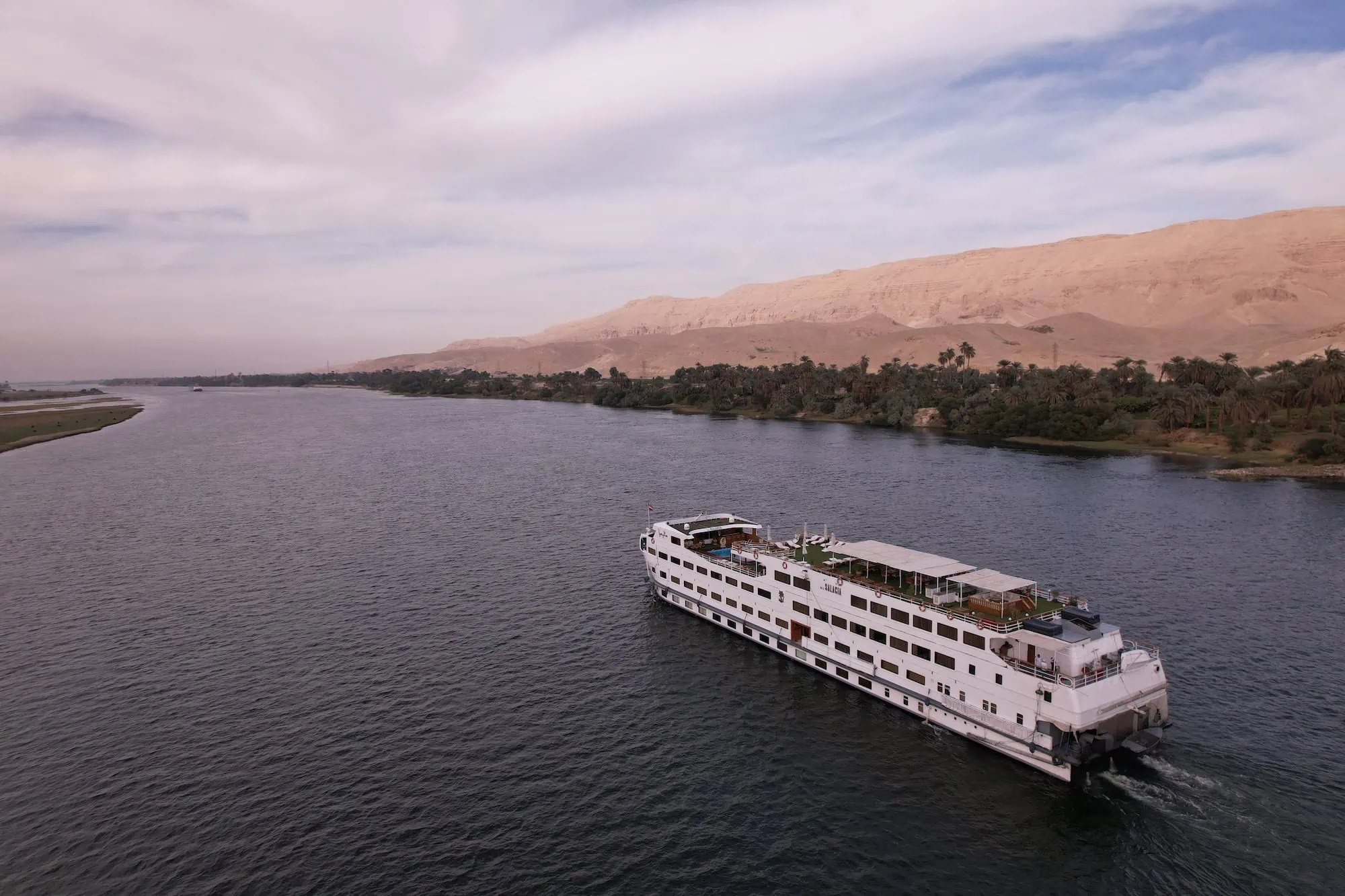 Aerial view of cruise ship sailing on the Nile River with desert cliffs and palm trees