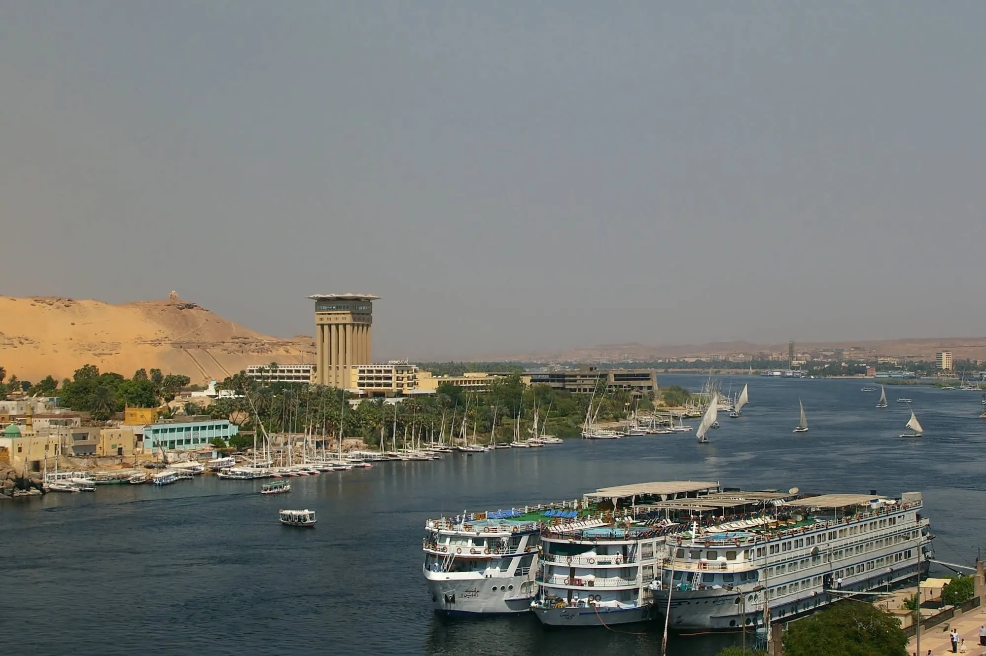 Cruise ships docked along the Nile River waterfront in Aswan with palm trees and desert cliffs