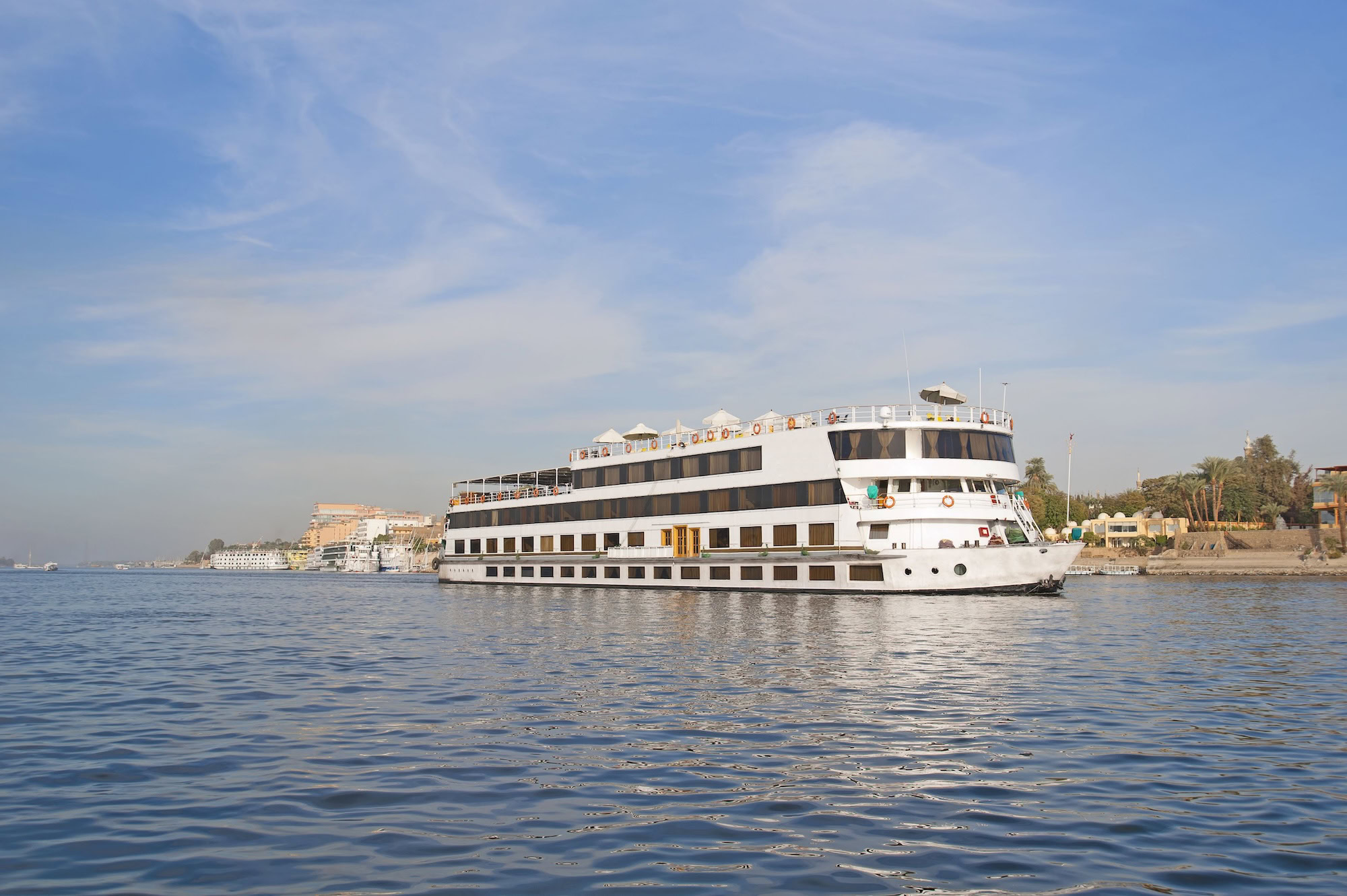 Nile River cruise ship in Aswan with palm trees and buildings