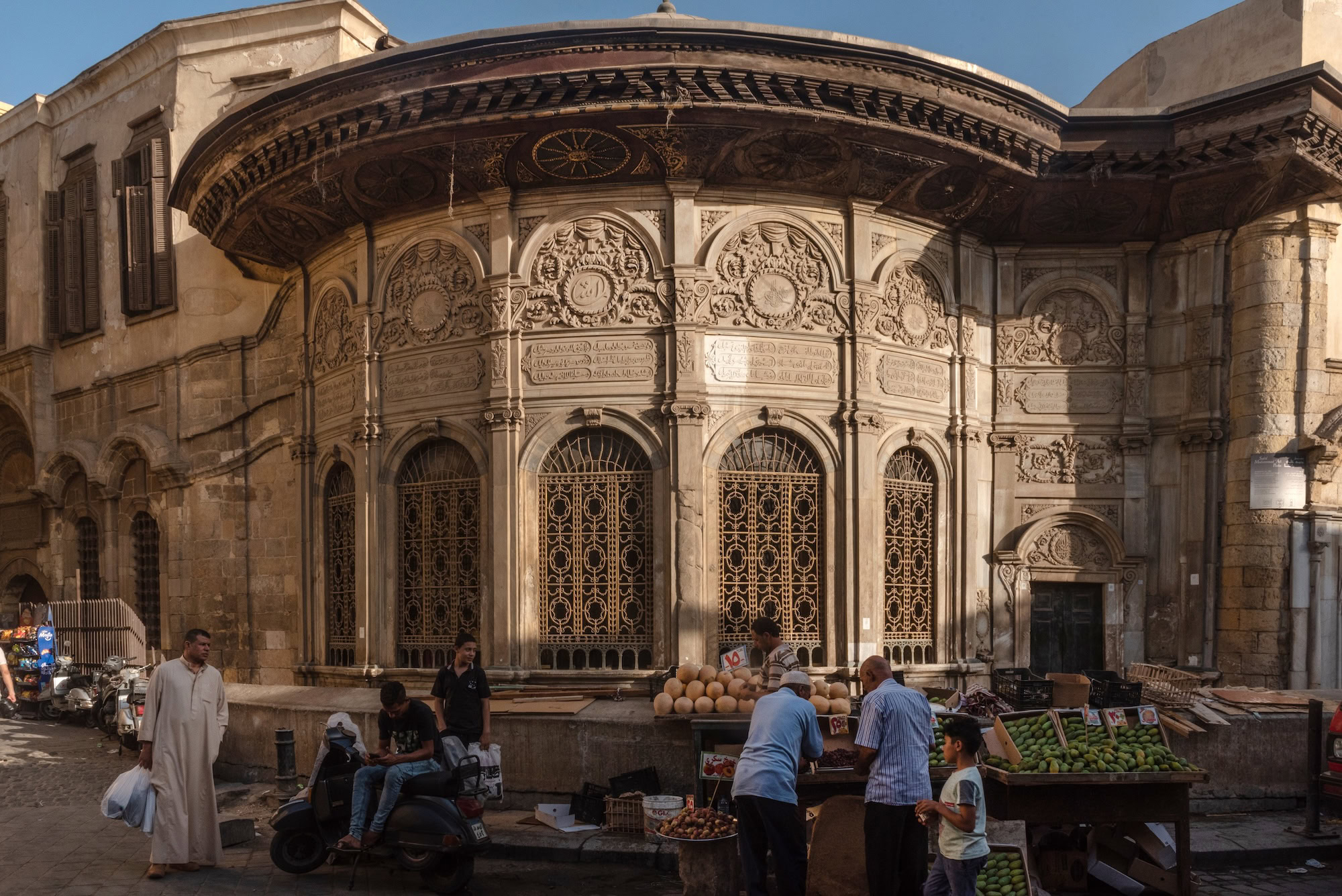 Bustling street scene in Cairo with historic mosque, fruit vendors and market activity