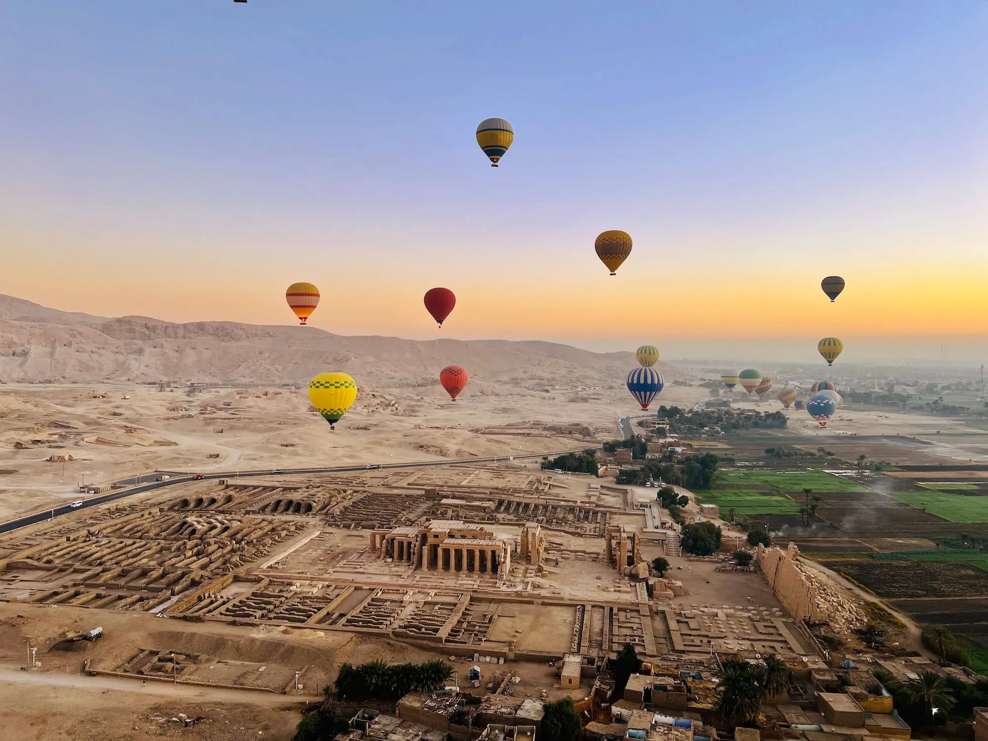 Aerial view of Valley of the Kings archaeological site with colorful hot air balloons floating above ancient ruins