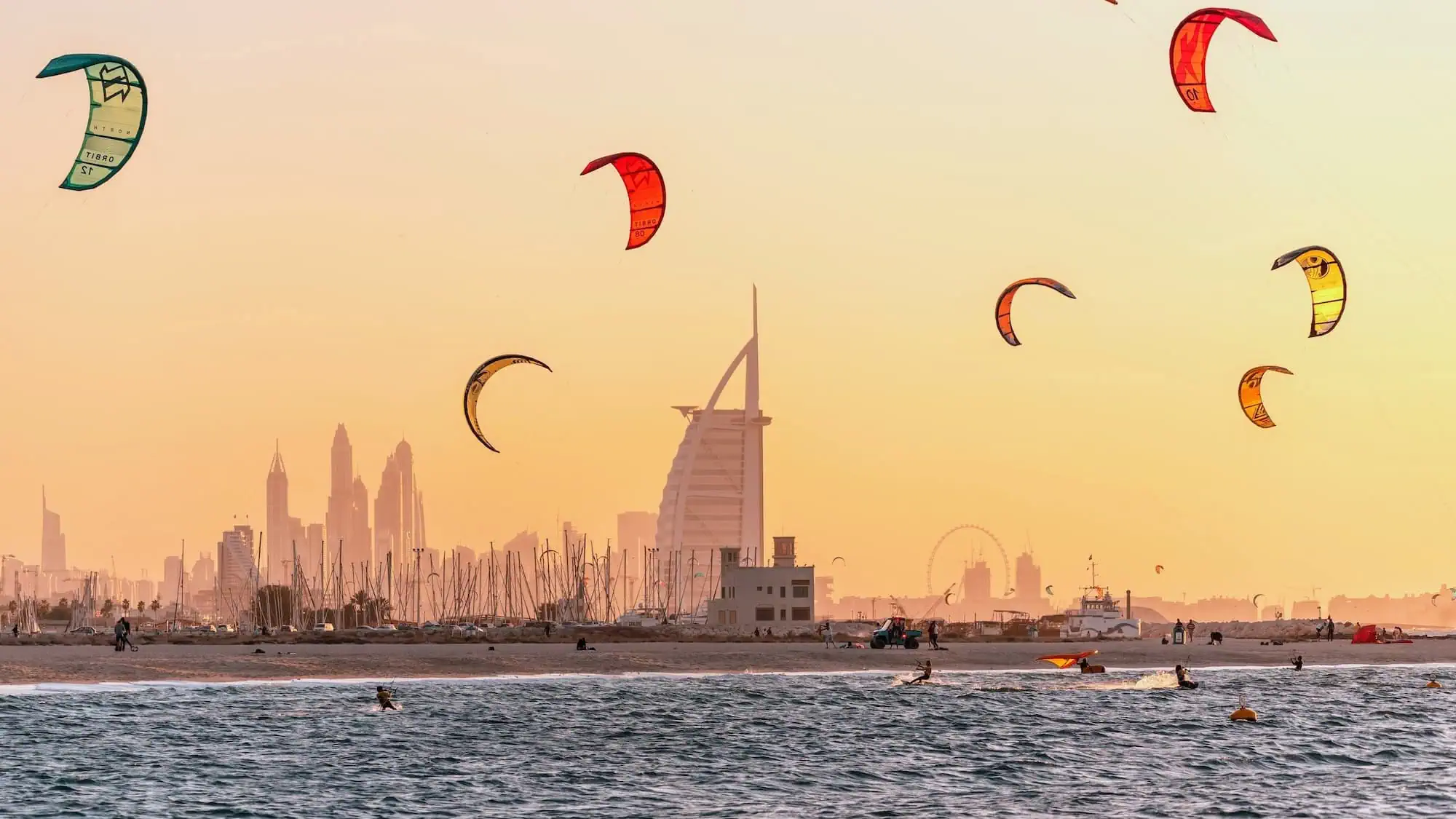 Colorful kitesurfing kites flying over Kite Beach Dubai at golden hour with city skyline