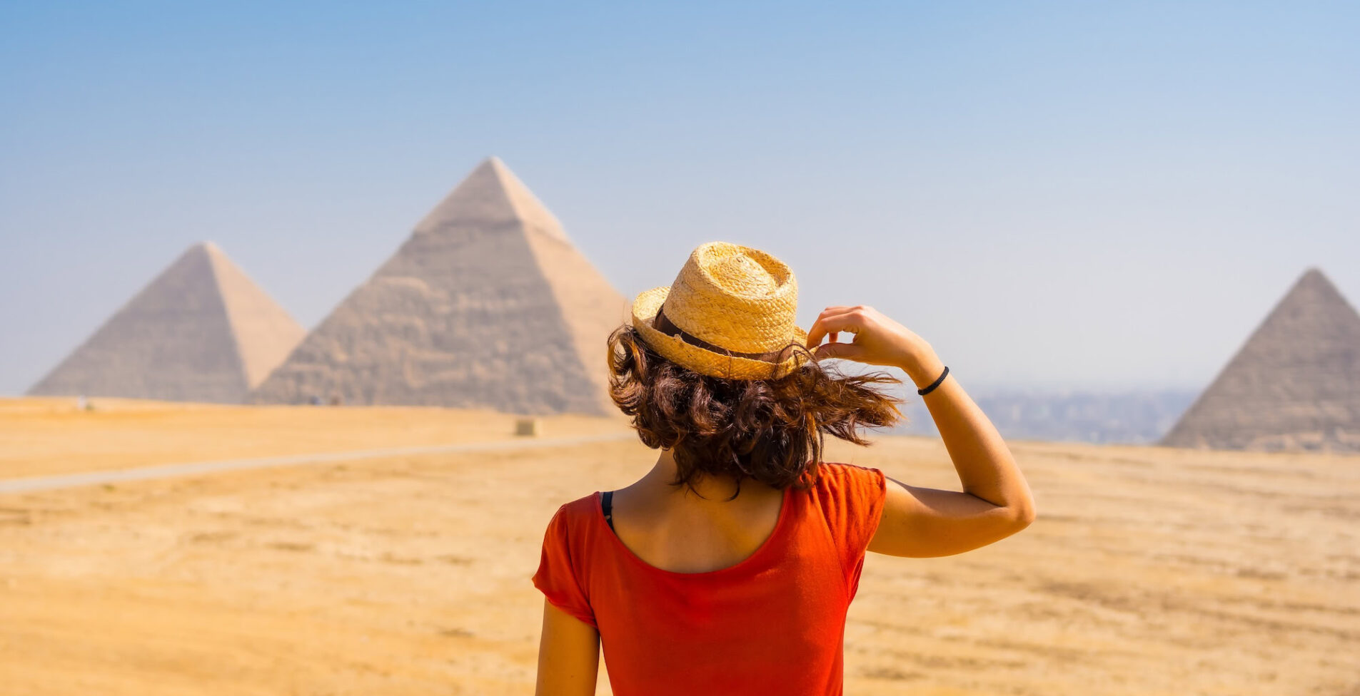 A young tourist in a red dress looking at the Pyramids of Giza the oldest Funerary monument in the world. In the city of Cairo Egypt