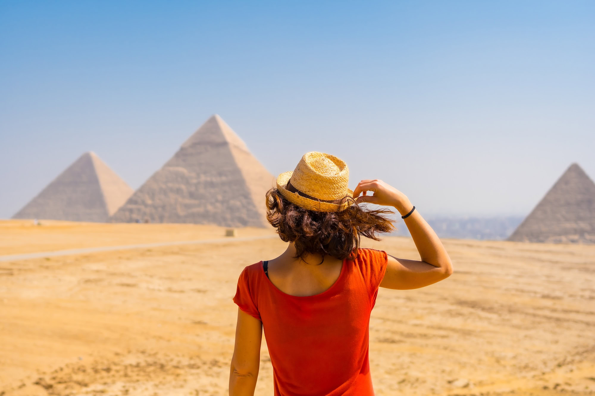 A young tourist in a red dress looking at the Pyramids of Giza the oldest Funerary monument in the world. In the city of Cairo Egypt