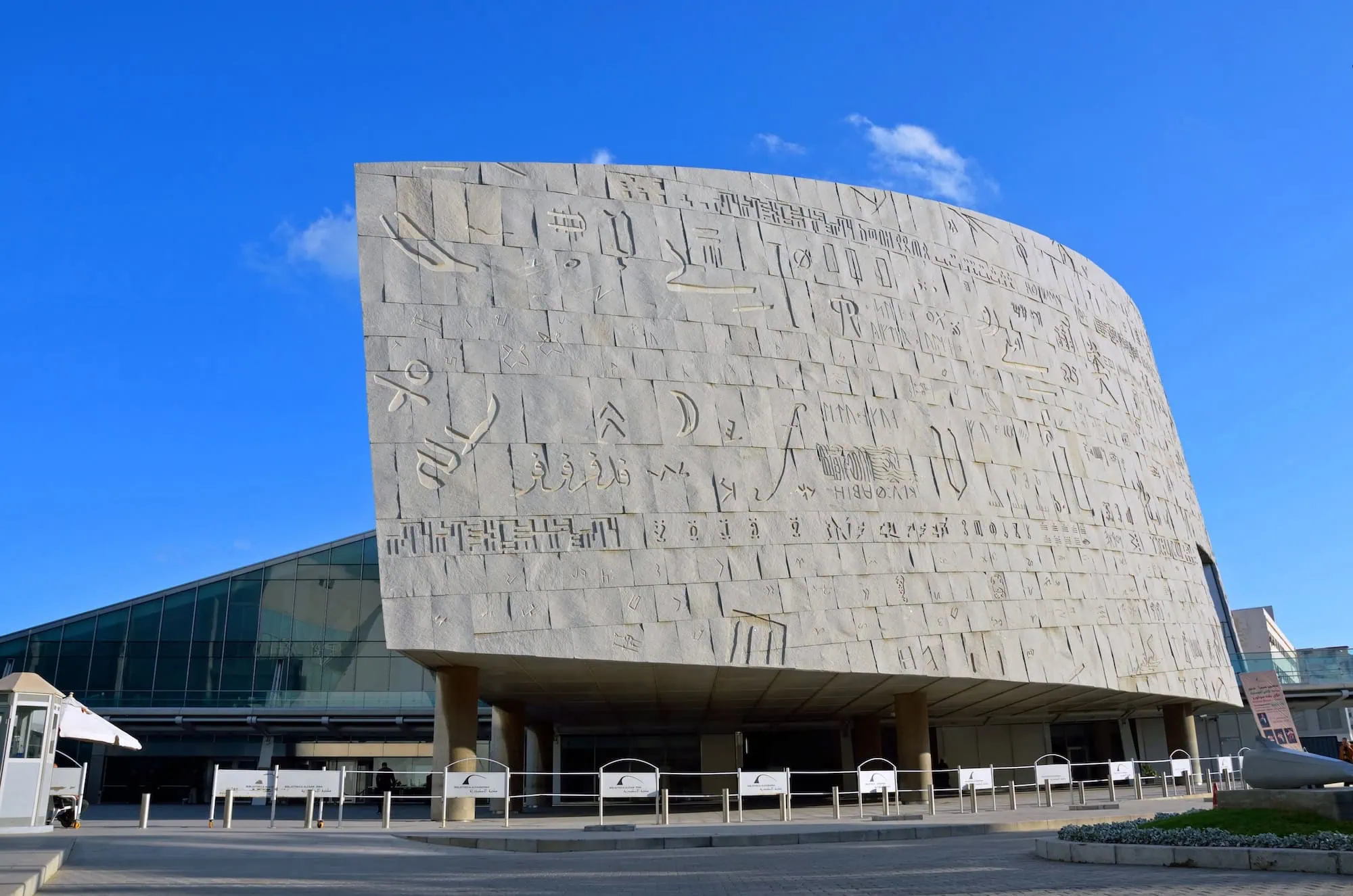 Modern Bibliotheca Alexandrina library building with glass facade and ancient hieroglyphic inscriptions on stone wall