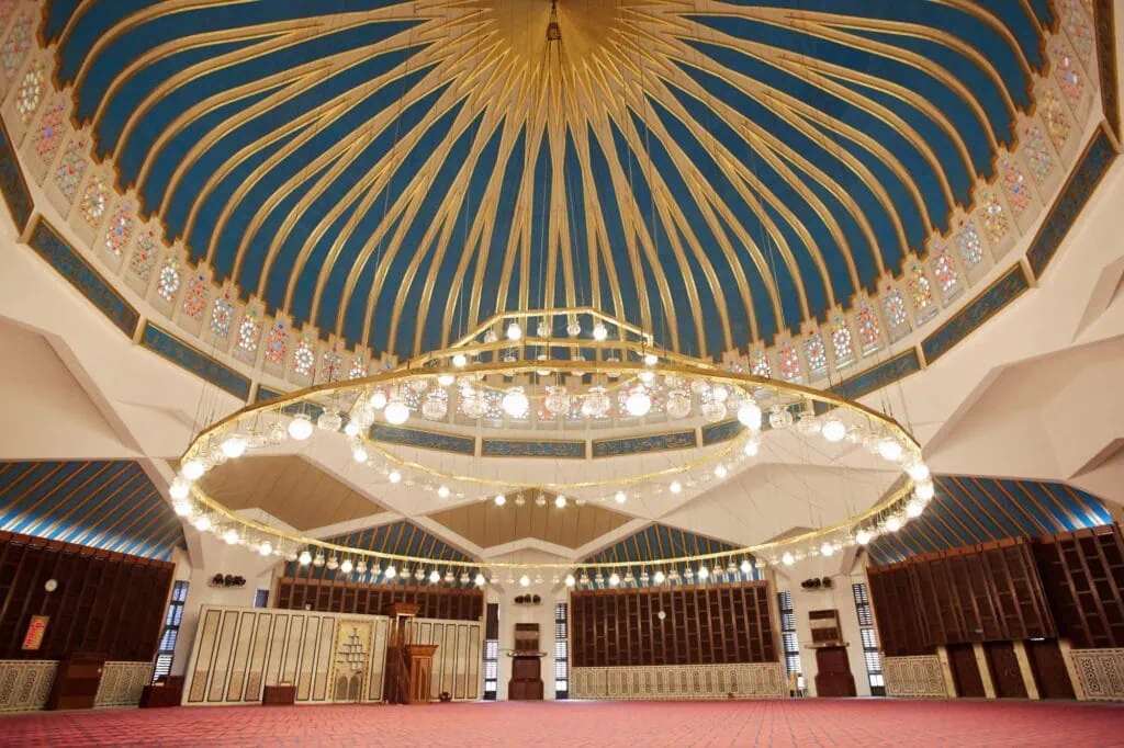King Abdullah I Mosque interior with blue dome, prayer hall, chandeliers, and carpeted floor Amman