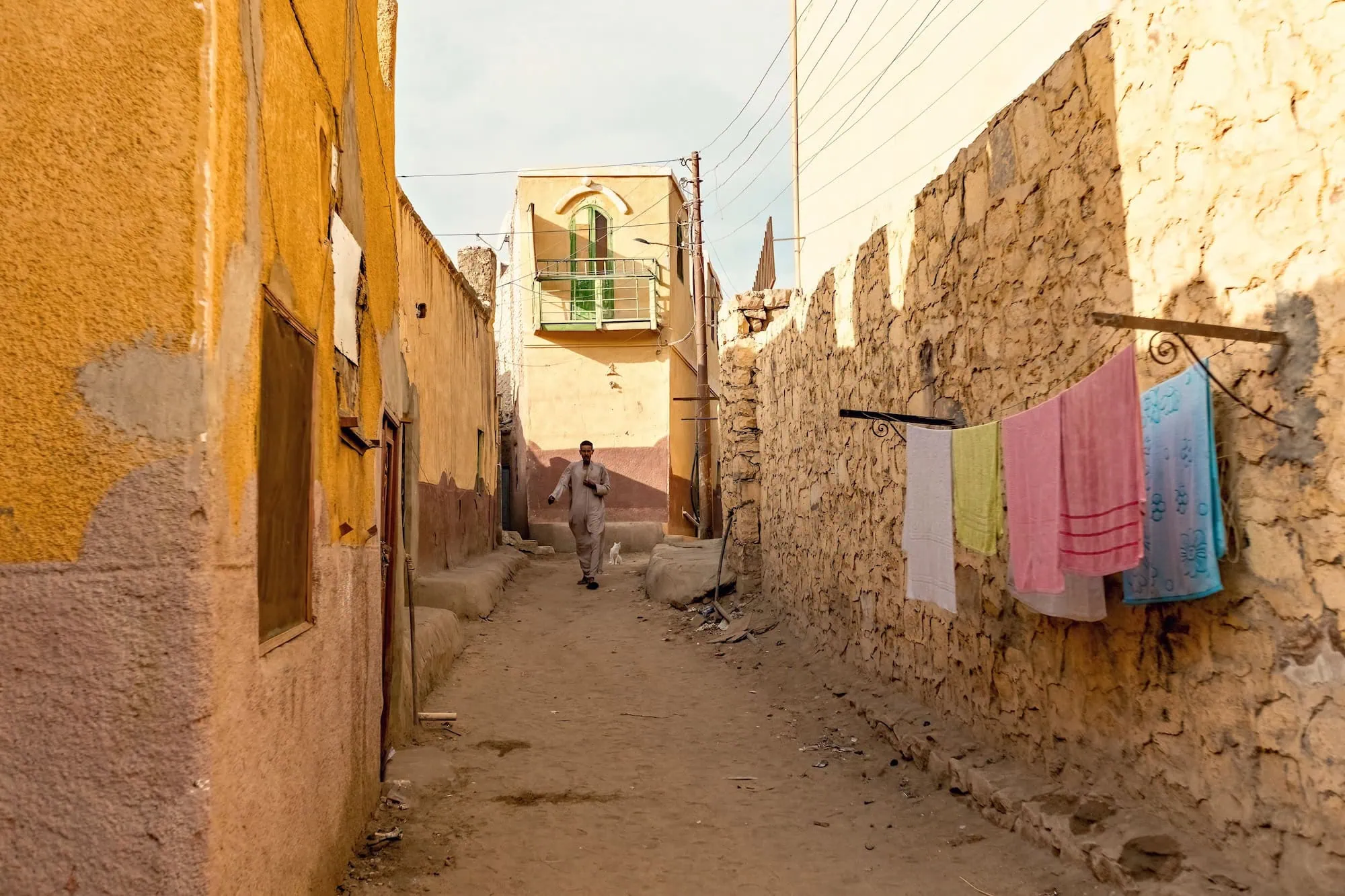Person in traditional white clothing walking through colorful Nubian village street in Aswan