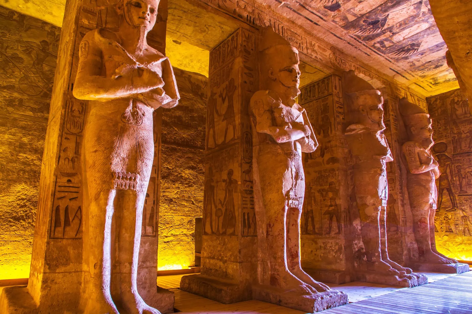 Rock-cut halls with colossal seated statues inside Abu Simbel Temple with warm golden lighting