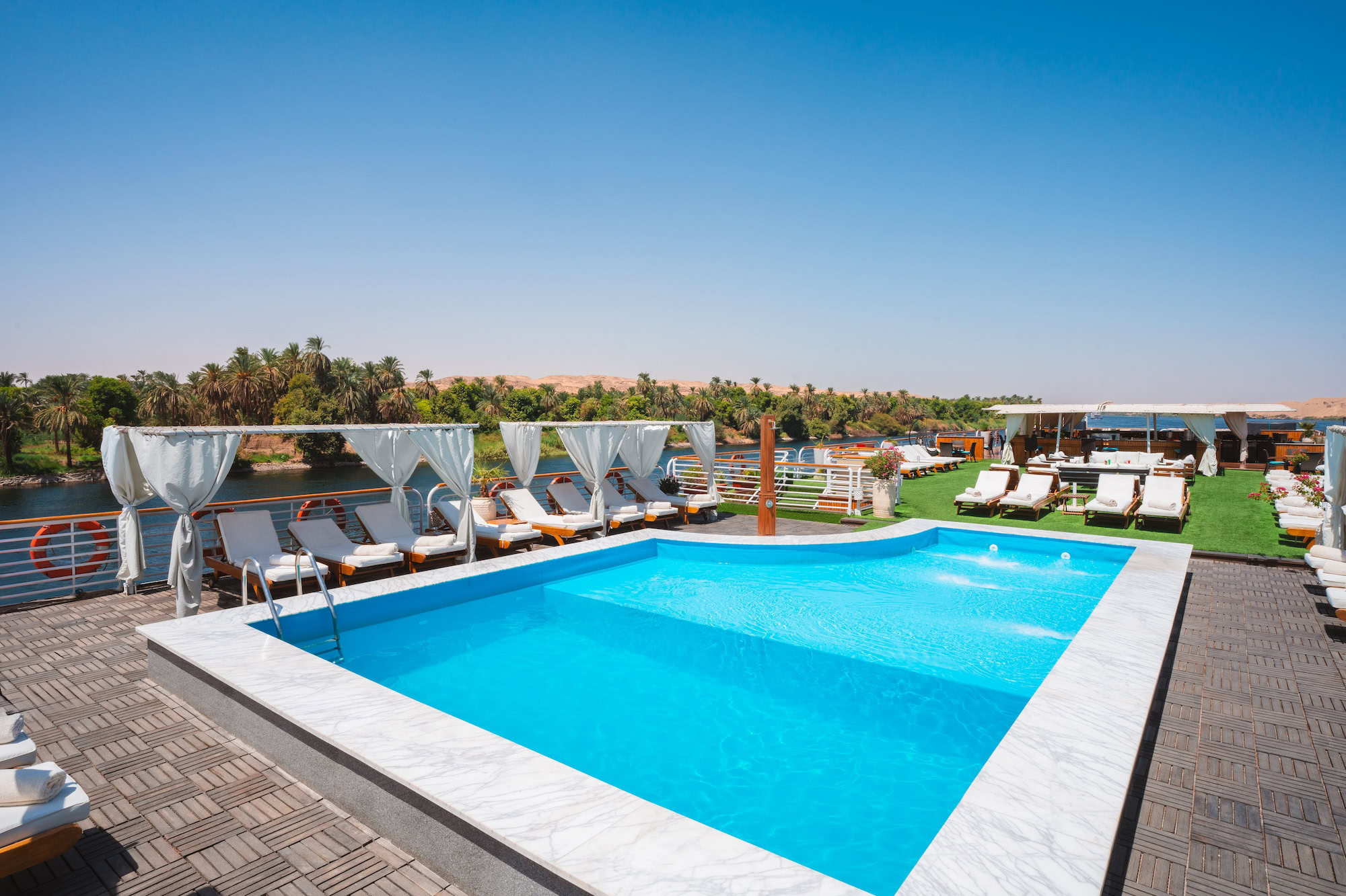 Luxury Nile cruise ship deck with swimming pool and lounge chairs overlooking the river