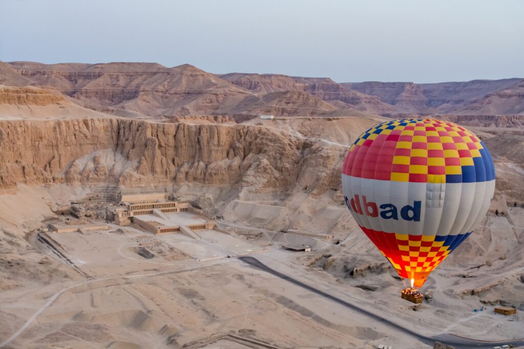 Aerial view of Hatshepsut Temple carved into the cliffs with a hot air balloon floating above, Luxor