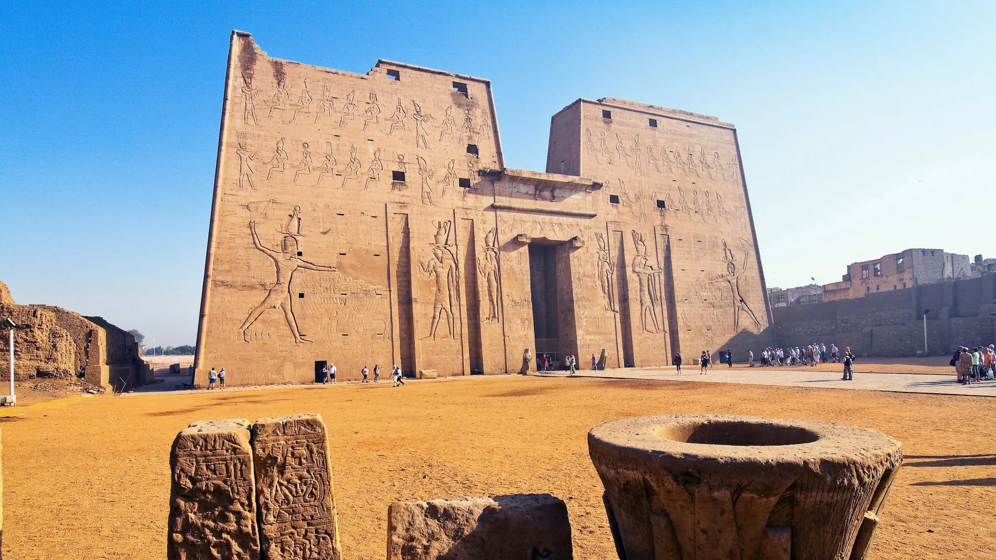 Templo de Edfu com hieróglifos, colunas de pedra e turistas explorando as ruínas antigas
