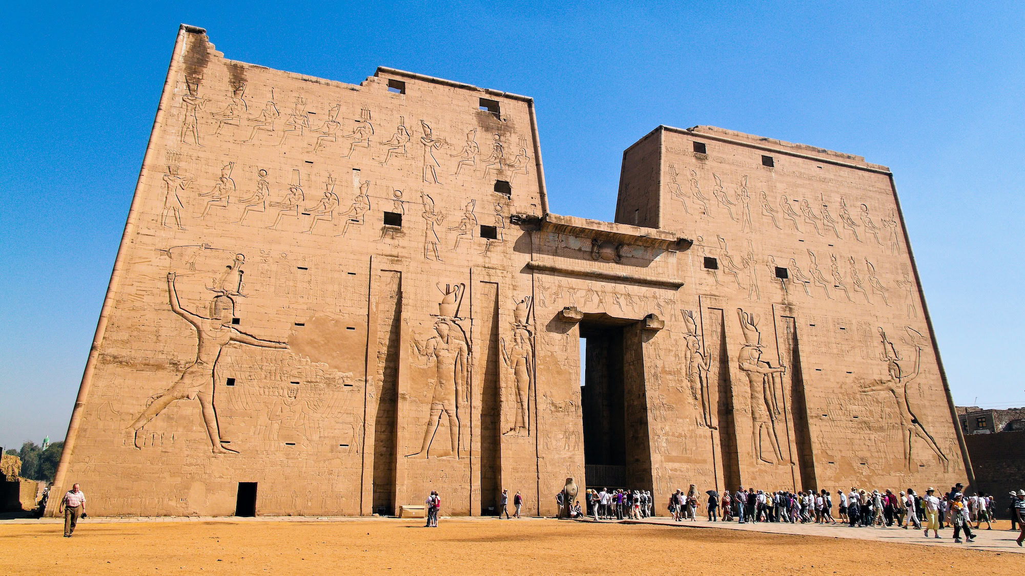 Tourists visiting Temple of Edfu entrance with ancient Egyptian hieroglyphics and carved reliefs