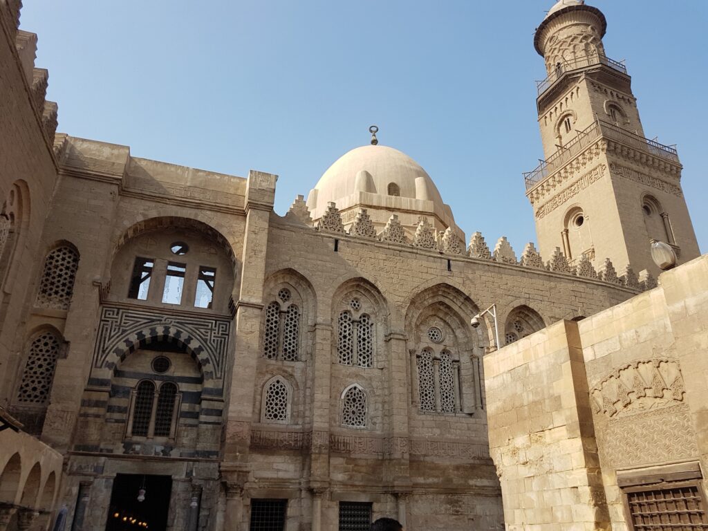 An exterior view of the carved stone facade with geometric reliefs of Al-Aqmar Mosque along Al-Muizz Street, Cairo