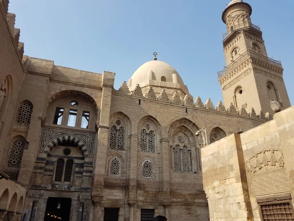 An exterior view of the carved stone facade with geometric reliefs of Al-Aqmar Mosque along Al-Muizz Street, Cairo