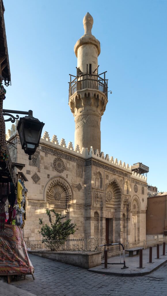 A morning street view along Al-Muizz Street with historic buildings and the stone facade of Al-Aqmar Mosque in the Old City, Cairo