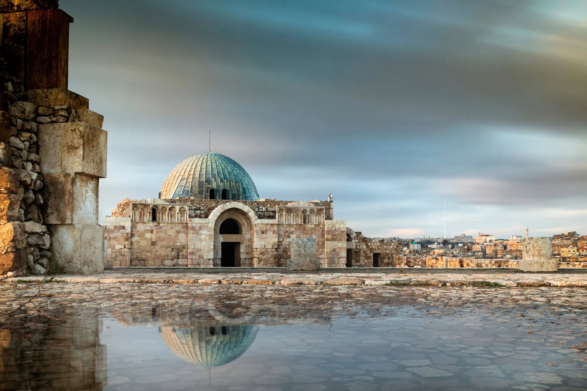 Ancient Amman Citadel ruins with blue dome reflected in water puddle
