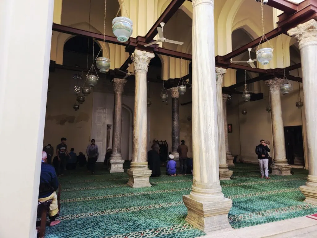 The prayer hall with stone columns, simple arches, and prayer carpets inside the Al-Aqmar Mosque, Cairo
