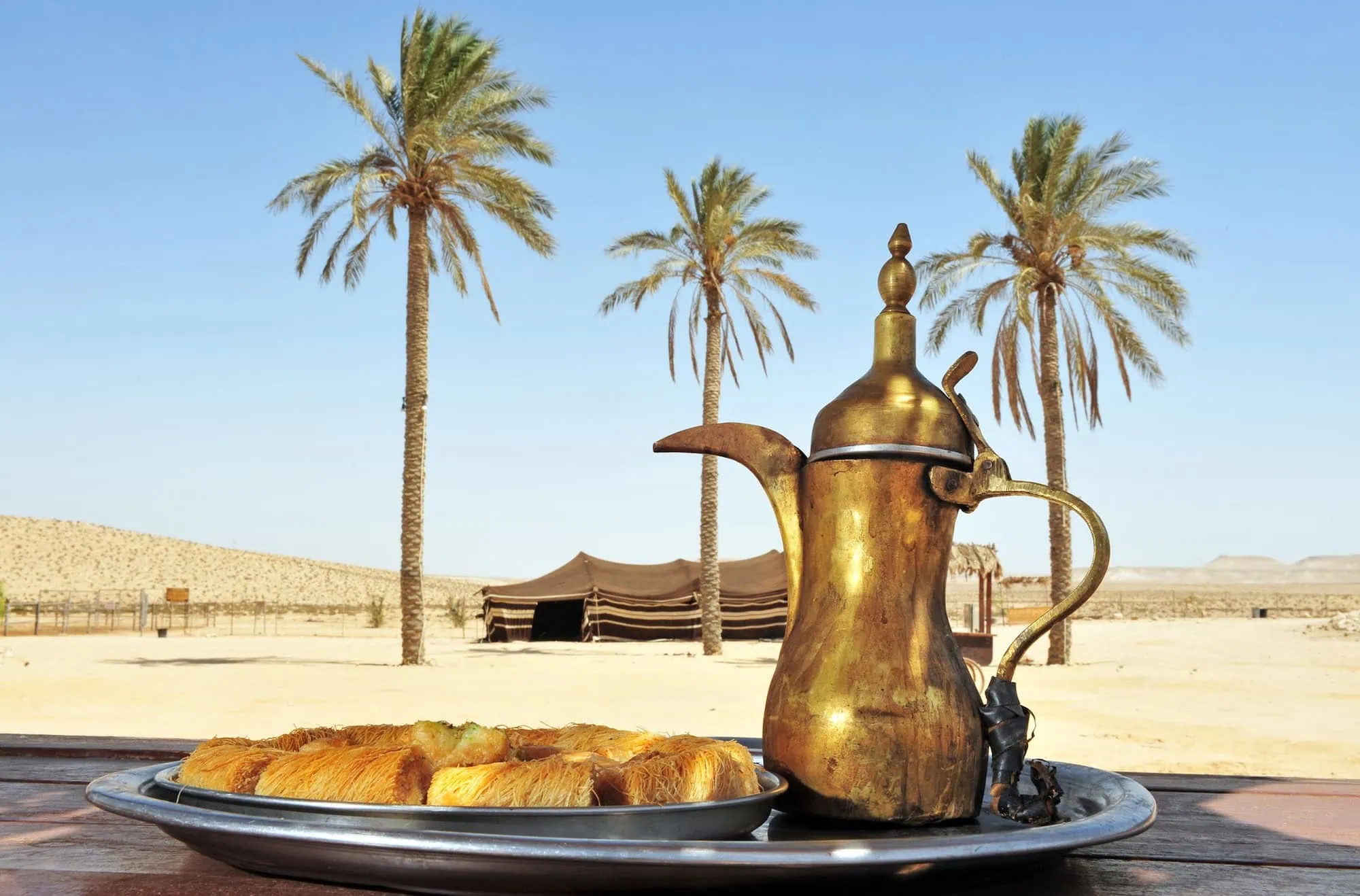 Traditional Arabic desert camp setup with coffee pot, dates, and tent in sand dunes