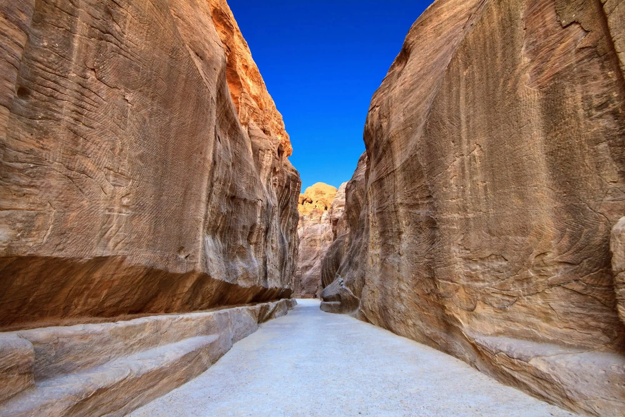 Narrow canyon passage with sandstone walls leading into Petra archaeological site