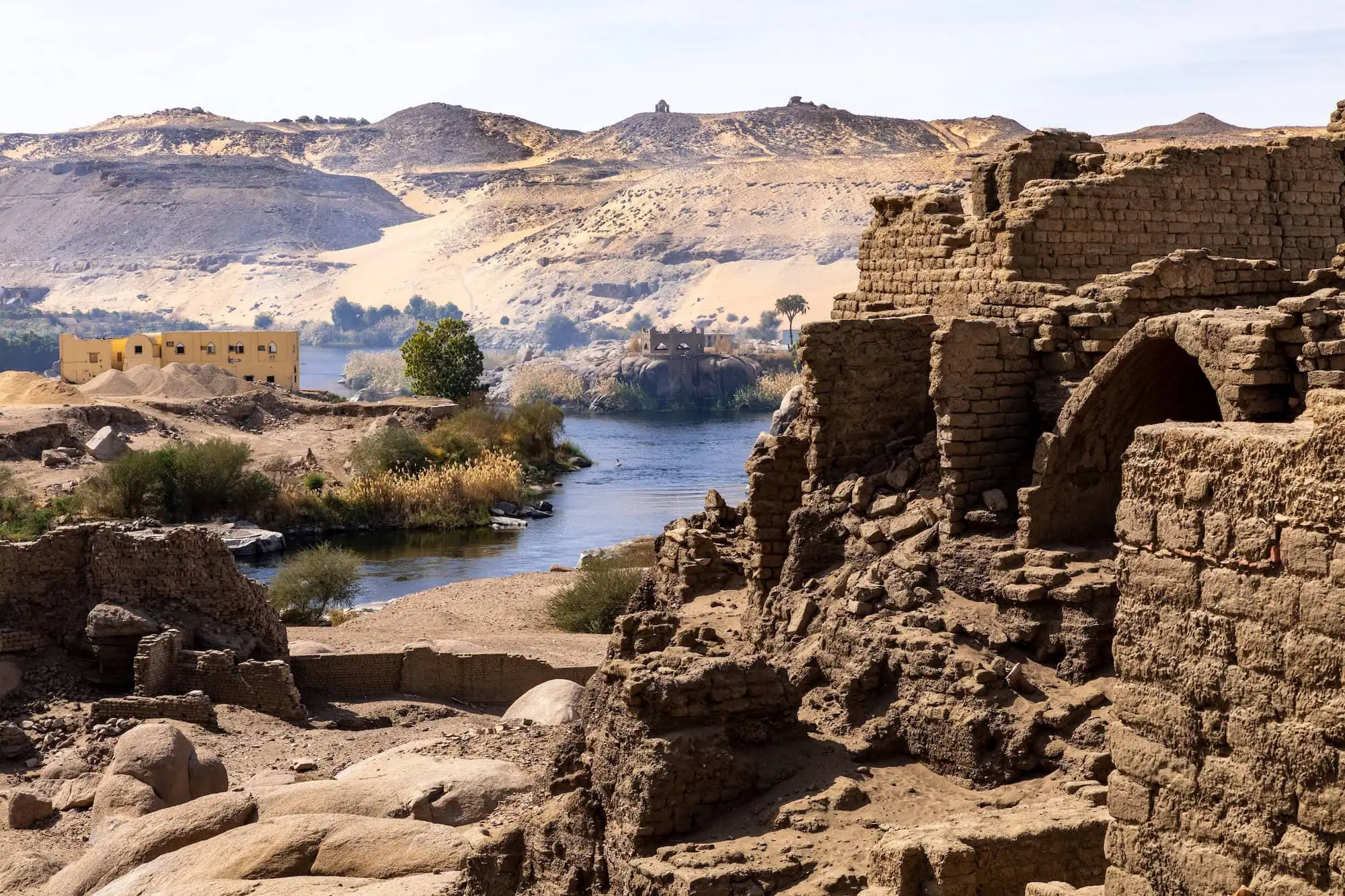 Ancient ruins with mud brick walls along the Nile River showing water infrastructure