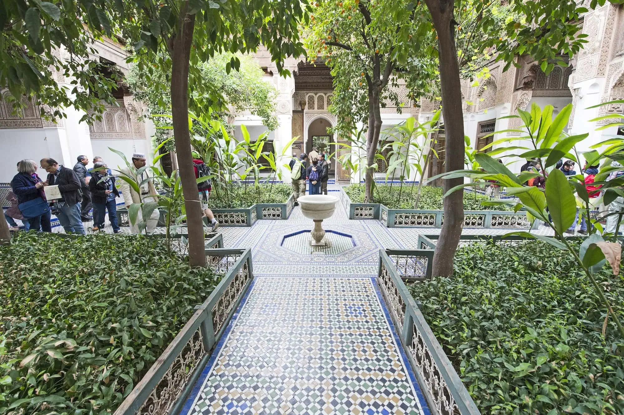 Tourists exploring the ornate courtyard of Bahia Palace with geometric fountain and lush gardens