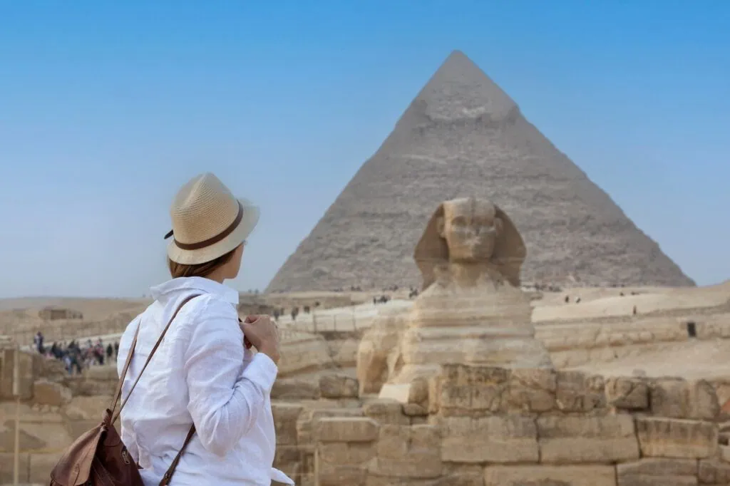 Back view of a woman wearing a hat looking toward the Great Sphinx and surrounding desert plateau, Giza