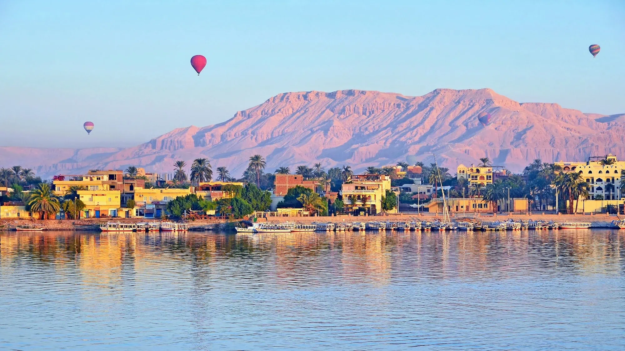 Hot air balloons floating above the Nile River at dawn in Luxor with golden morning light