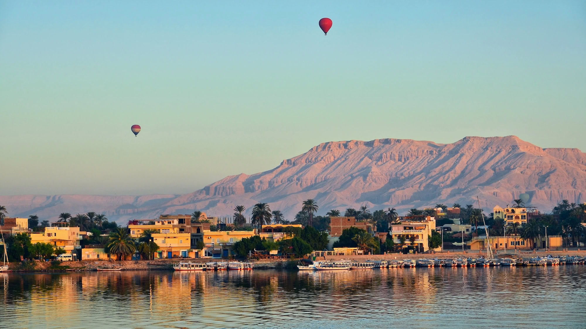 Hot air balloons floating over the Valley of Kings area with desert hills and the Nile River
