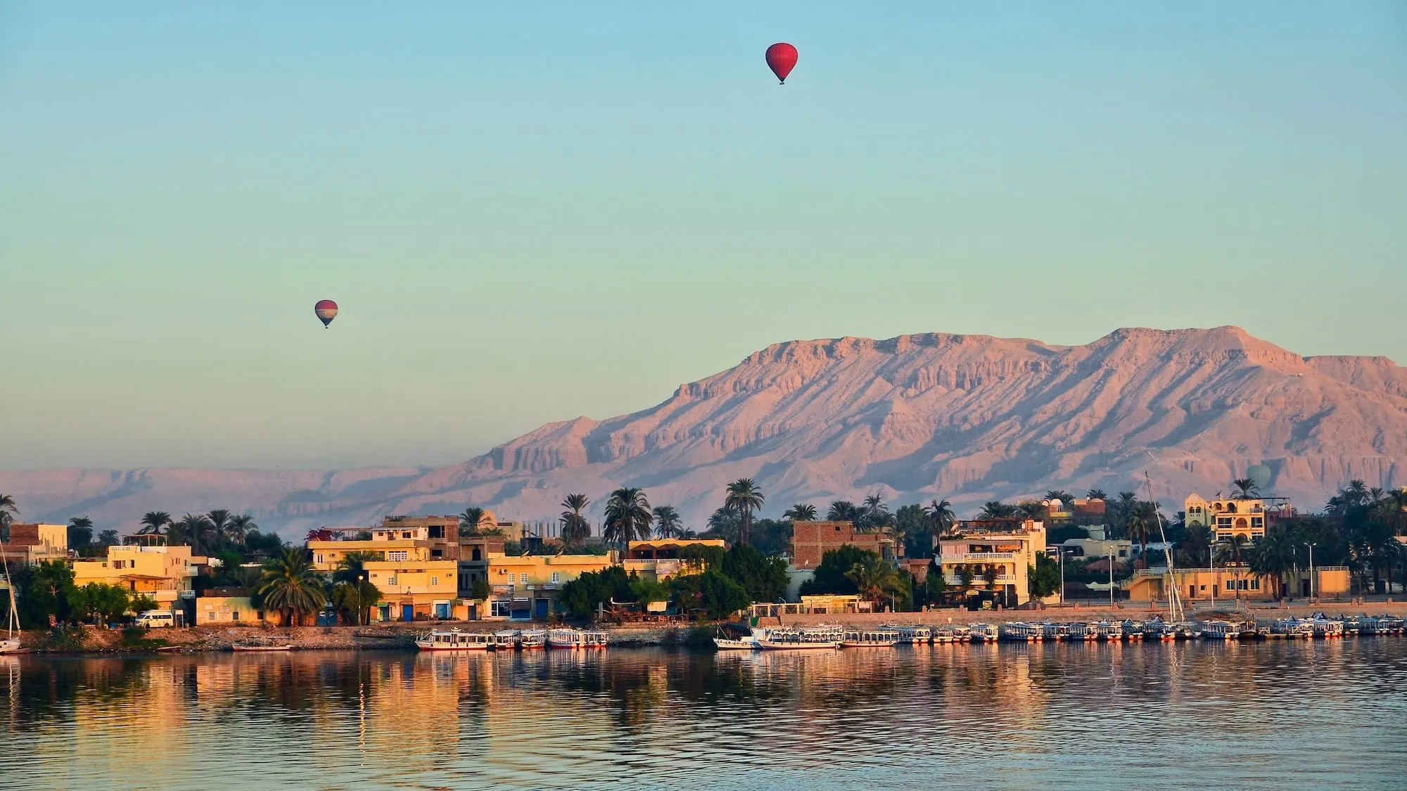 Hot air balloons floating over the Valley of Kings area with desert hills and the Nile River
