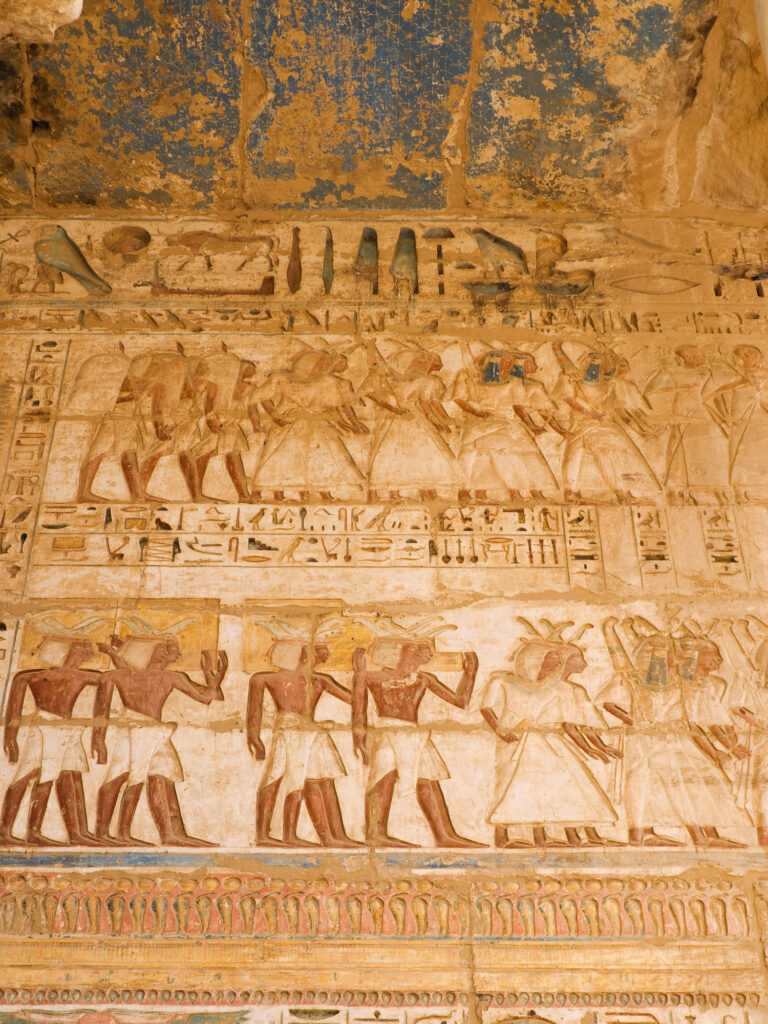 Bas-relief carvings depicting figures and hieroglyphs on stone walls at Medinet Habu Temple, Luxor