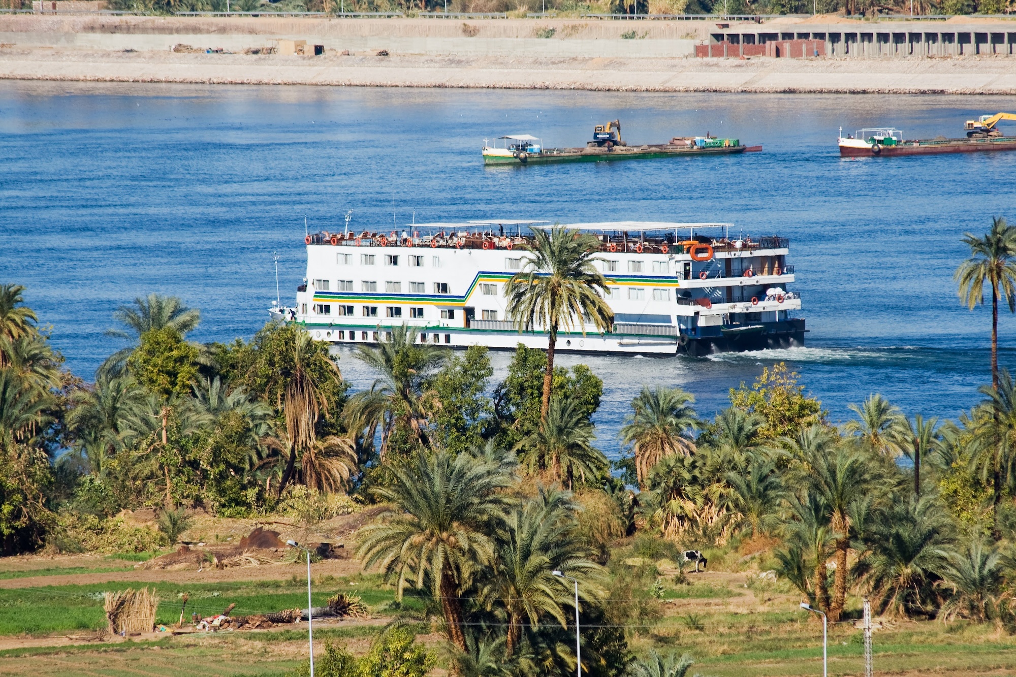 White Nile River cruise ship sailing past lush green palm trees and cultivated fields