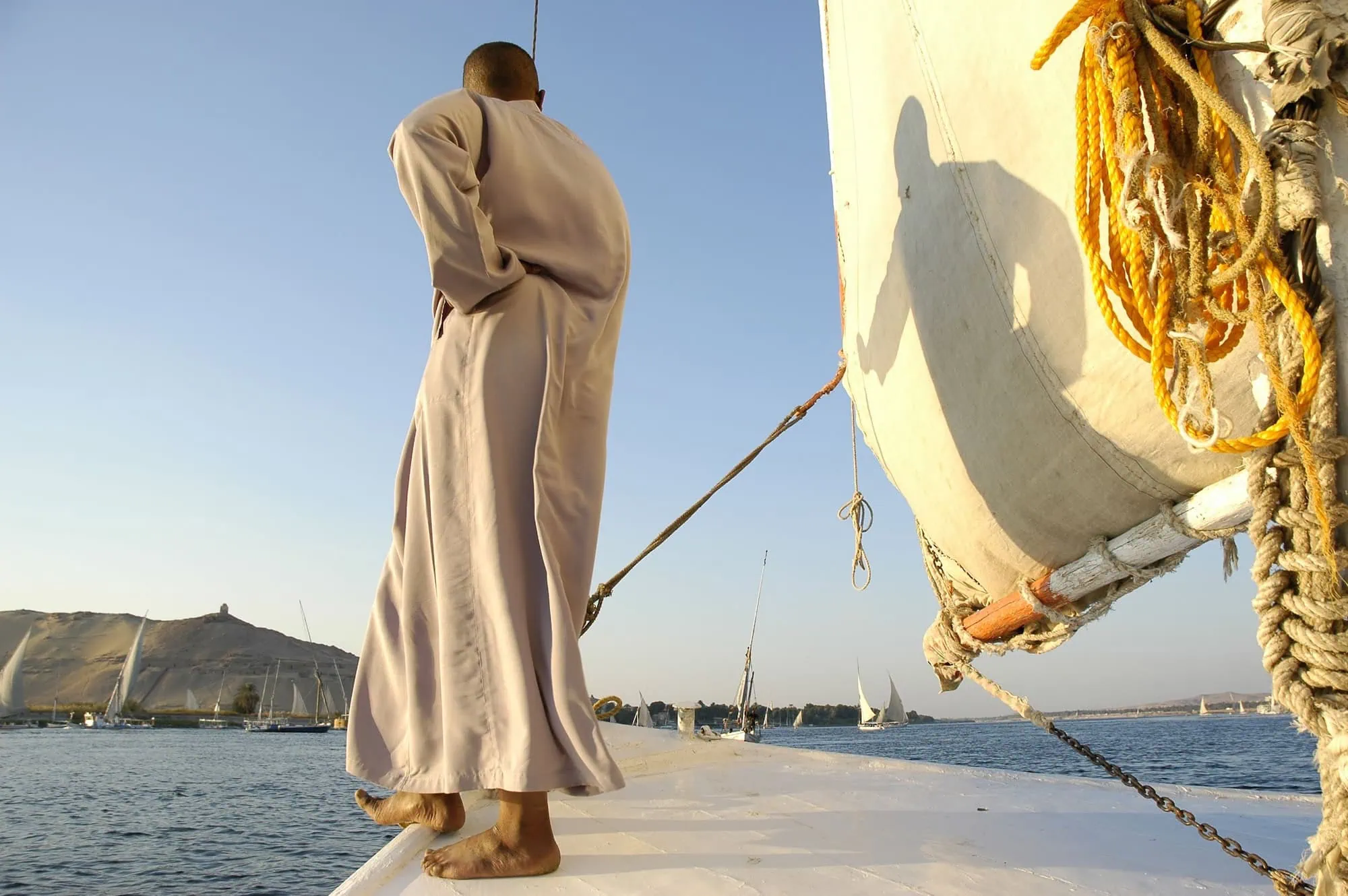 Man in traditional robe working on sailboat on Egyptian waters with scenic hills in background