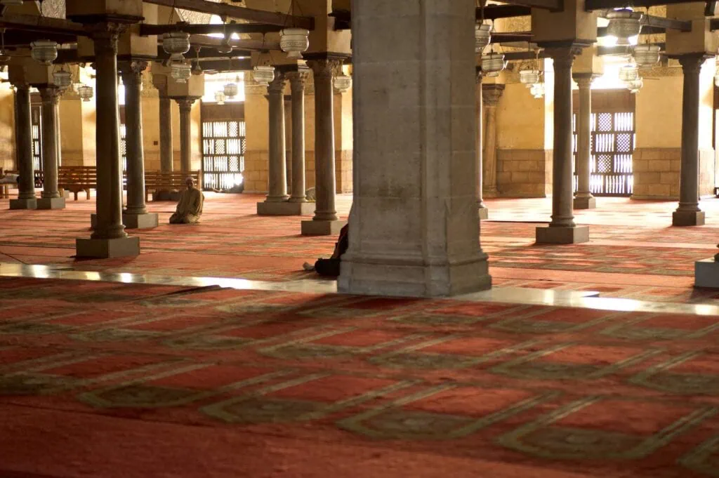 An interior view with columns, arches, chandeliers, and prayer carpets inside Al-Azhar Mosque, Cairo