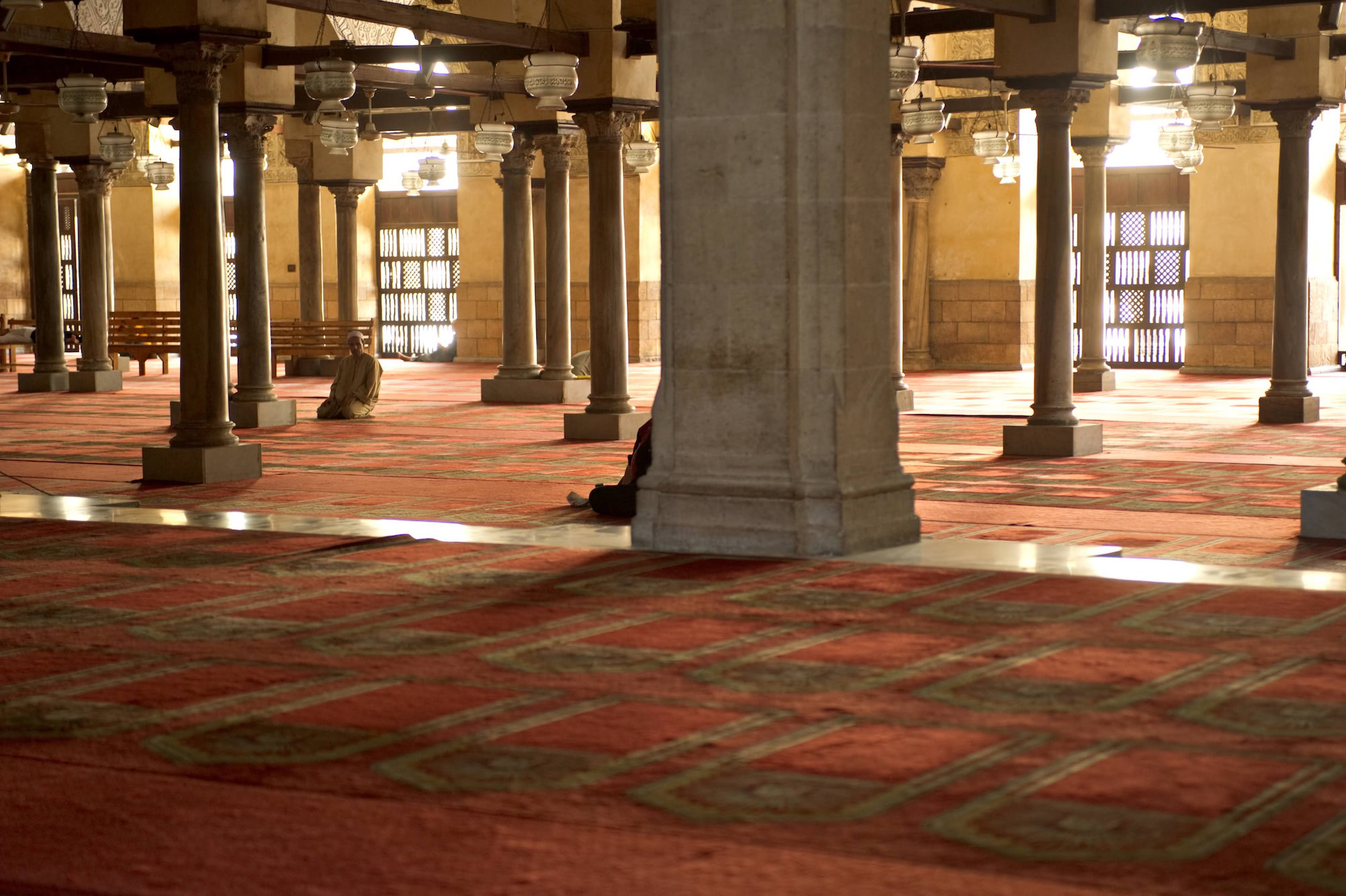 Interior prayer hall of Al-Azhar Mosque with stone columns and students studying
