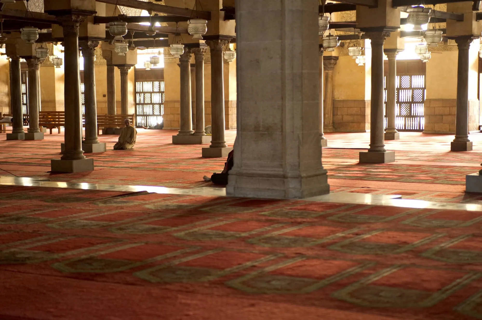 Interior prayer hall of Al-Azhar Mosque with stone columns and students studying