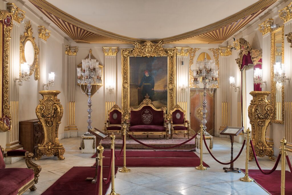 The Throne Hall with gold-plated red armchairs, ornate ceiling, antique floor lamps, and red carpets inside Manial Palace, Cairo