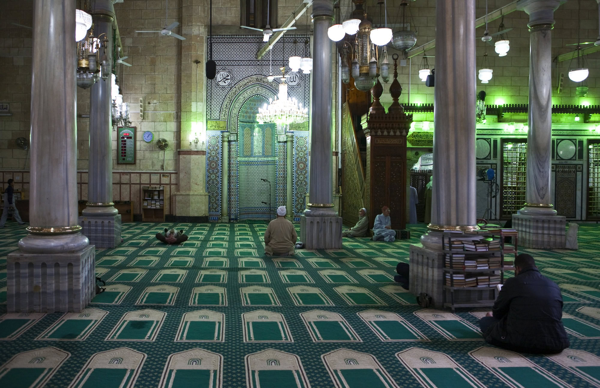 Worshippers praying respectfully in ornate mosque prayer hall with Islamic geometric patterns