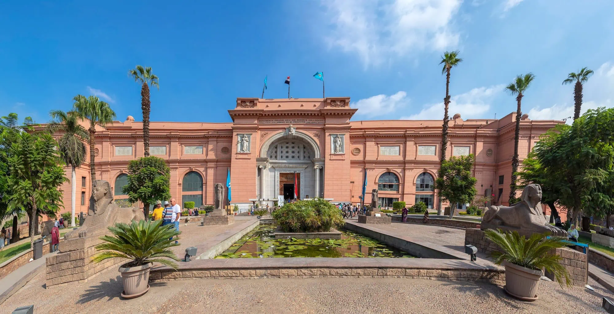 Egyptian Museum building with sphinx statues, palm trees, and tourists at entrance