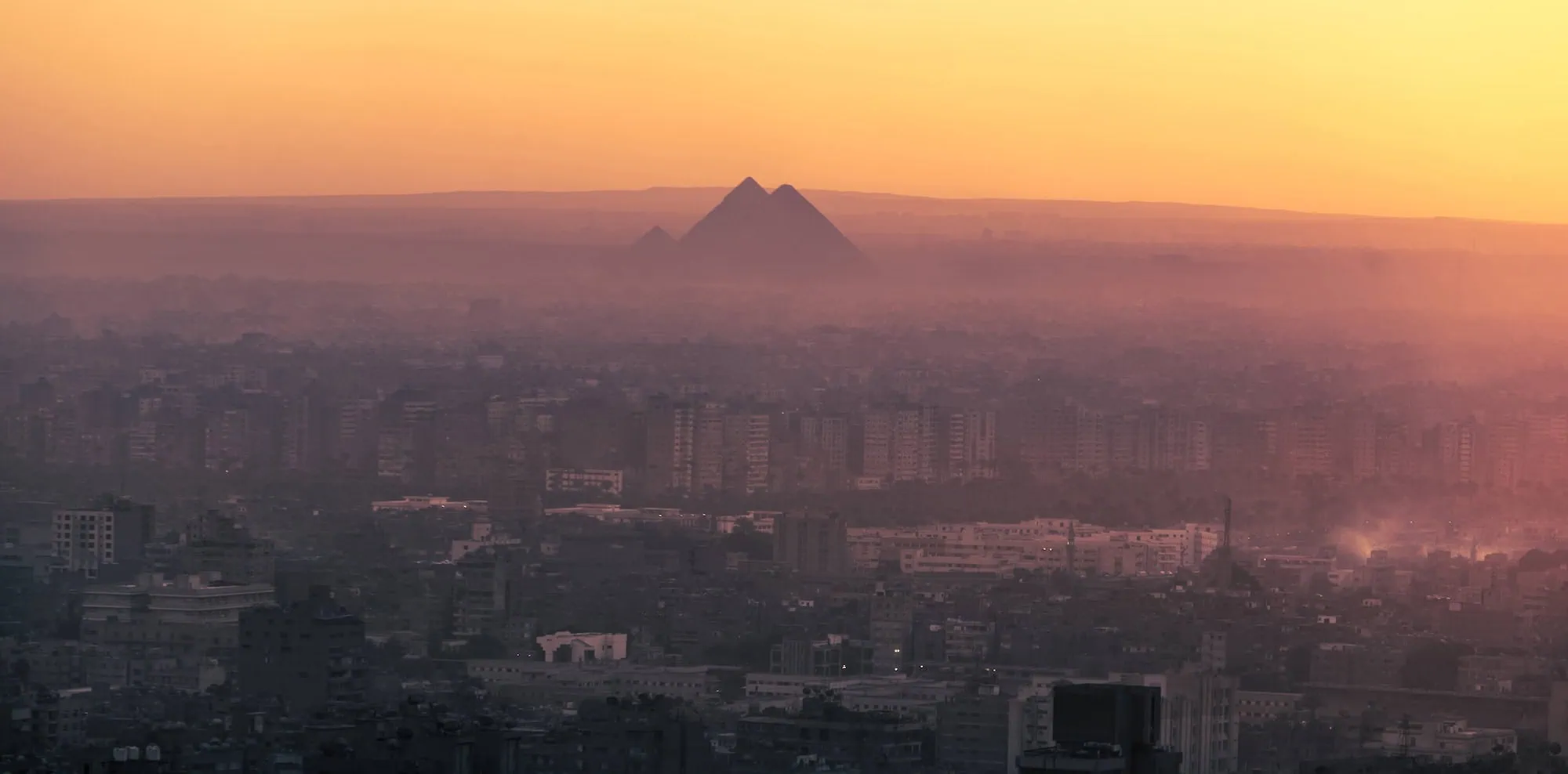 Cairo cityscape at sunset showing the iconic Giza pyramids in the distance