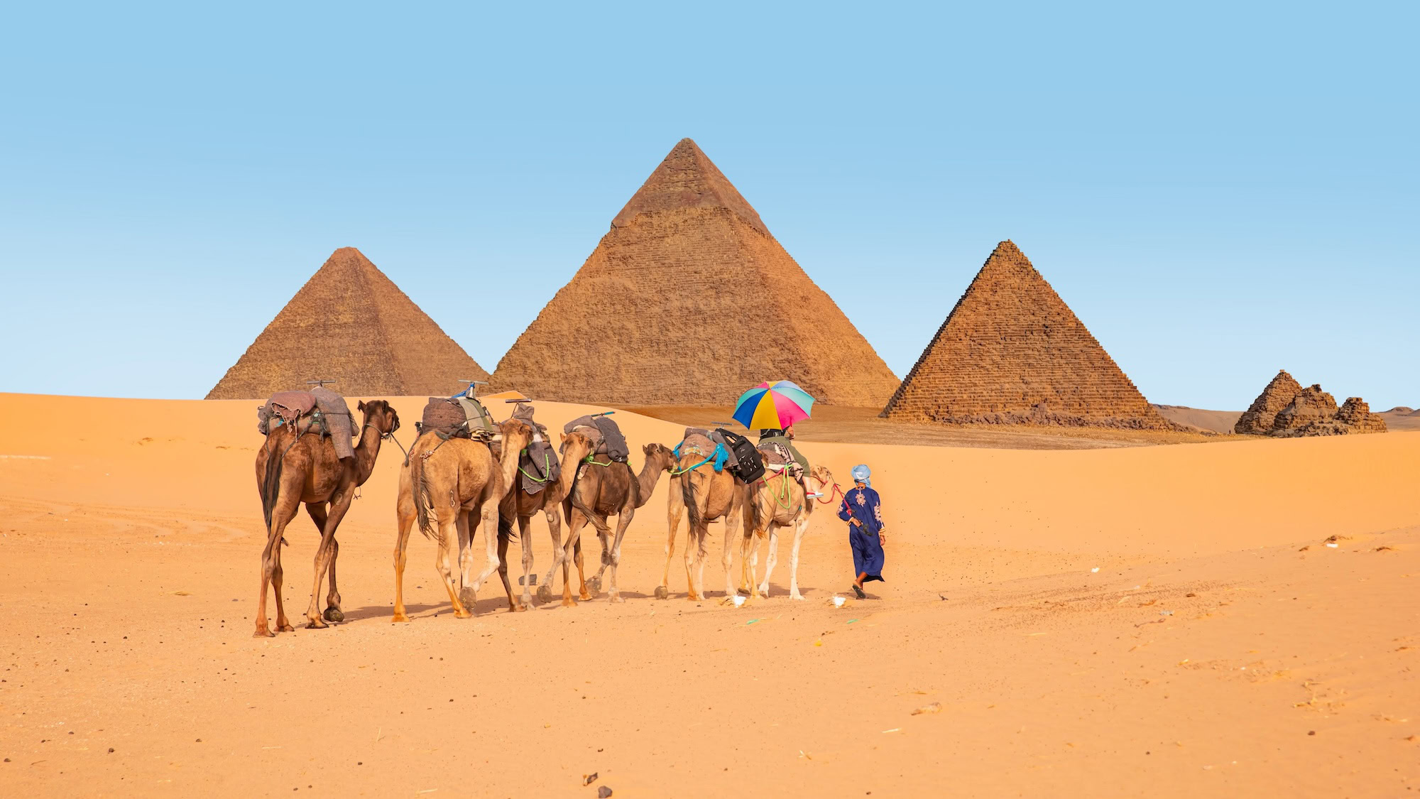 Pyramids of Giza with camel handlers using umbrella for shade in desert