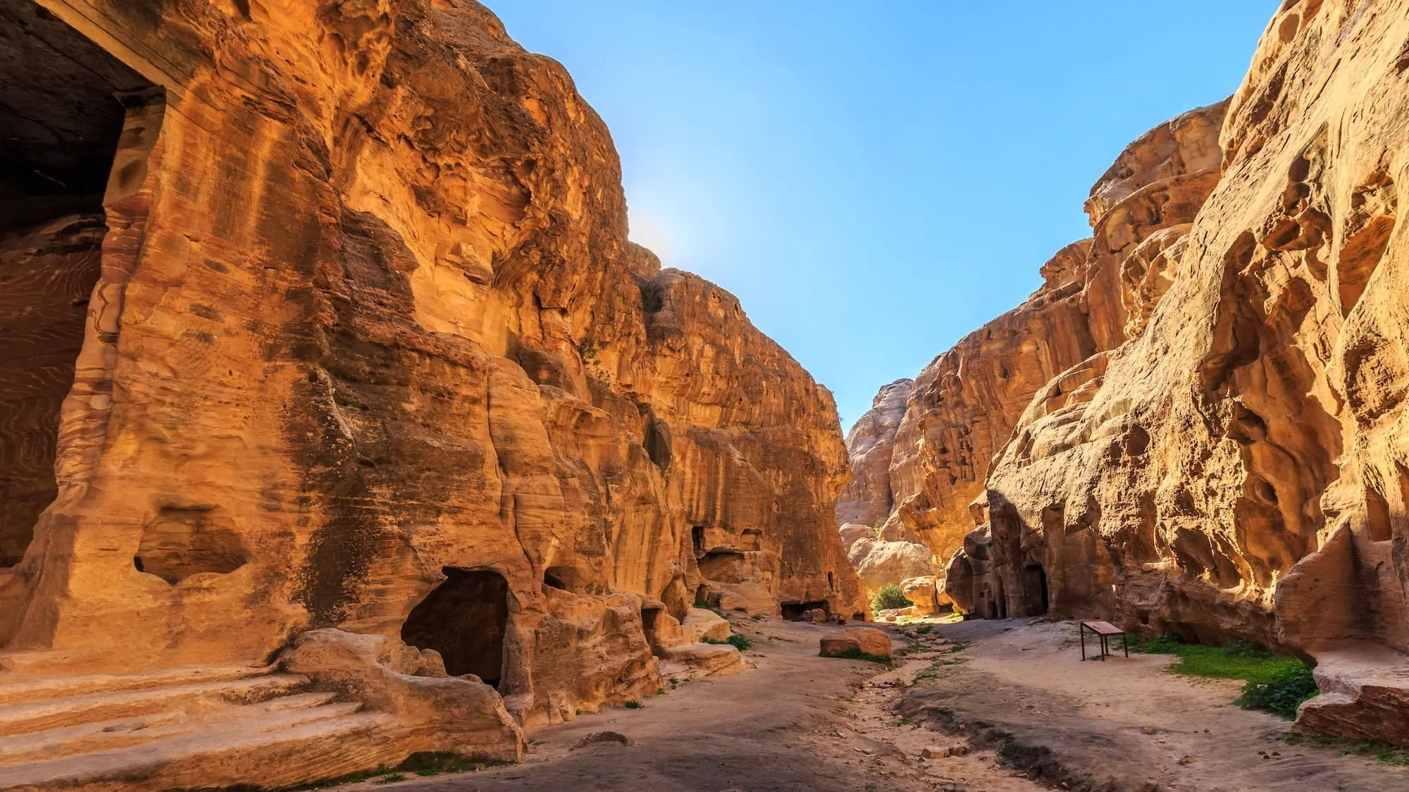 Ancient carved rock buildings and chambers in the golden sandstone cliffs of Little Petra