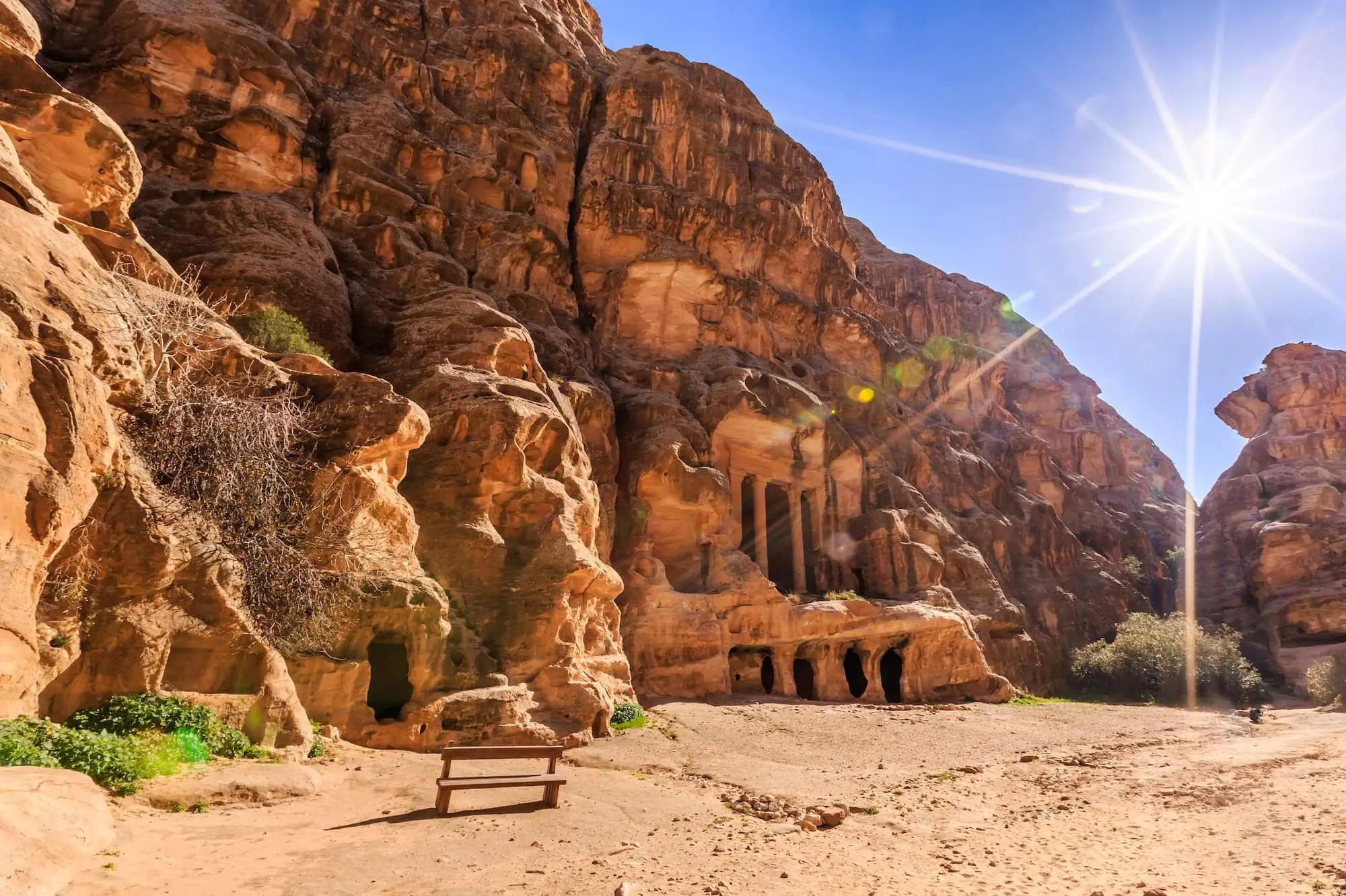 Ancient Nabataean carved buildings at Little Petra with red sandstone cliffs and wooden bench