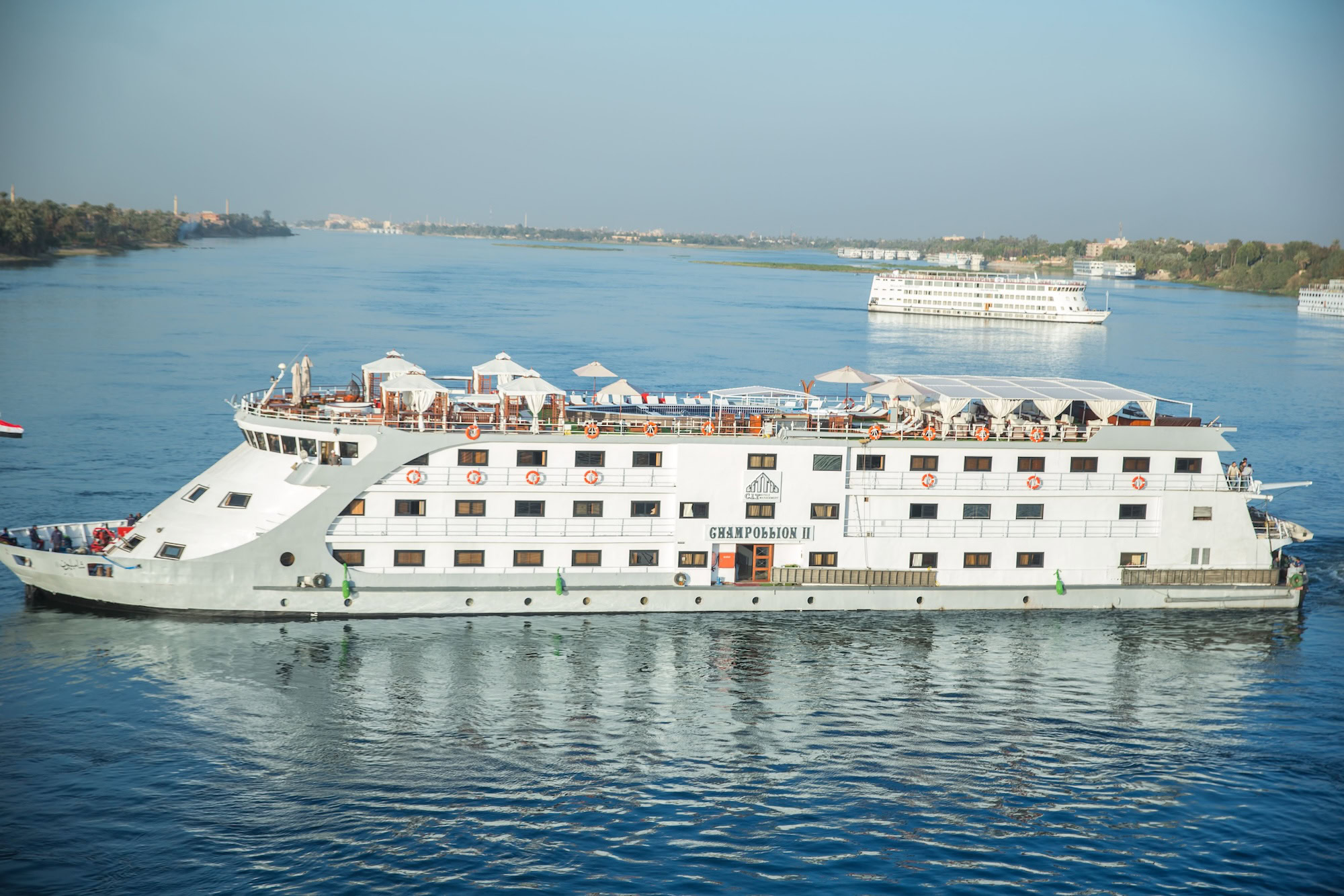 Cruise ship on the Nile River with buildings and vegetation along the shoreline