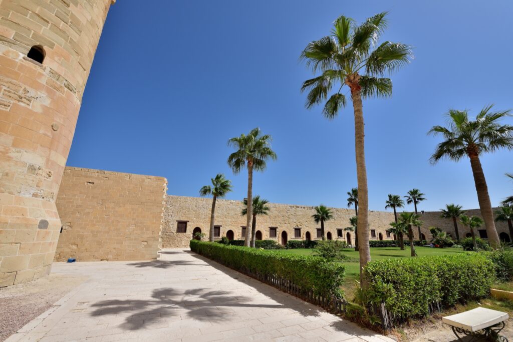 Central courtyard with palm trees, grass, and surrounding stone walls inside the Citadel of Qaitbay, Alexandria