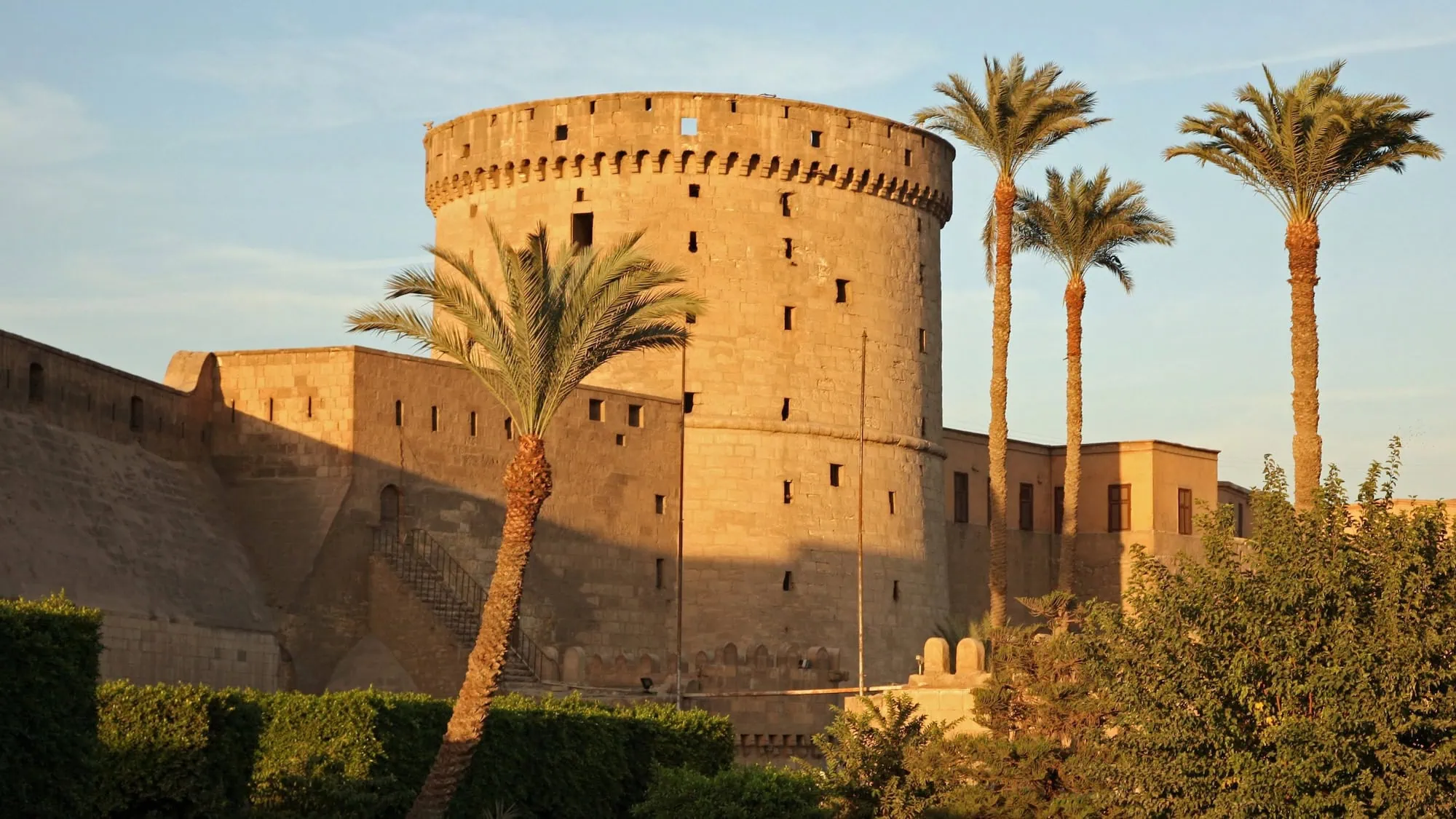 Round defensive tower of Saladin's Citadel in Cairo surrounded by fortress walls and palm trees