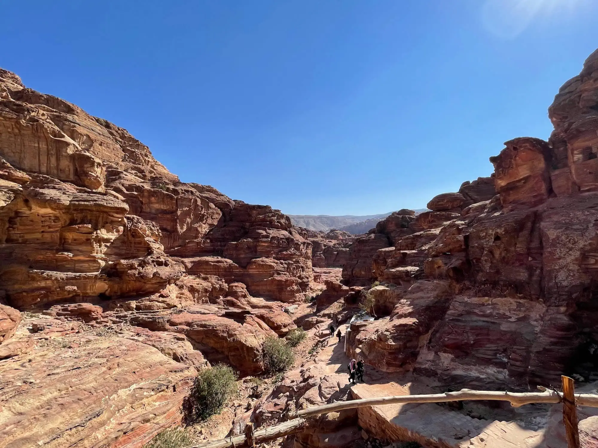 Tourists walking along rocky paths through red sandstone cliffs at Petra archaeological site