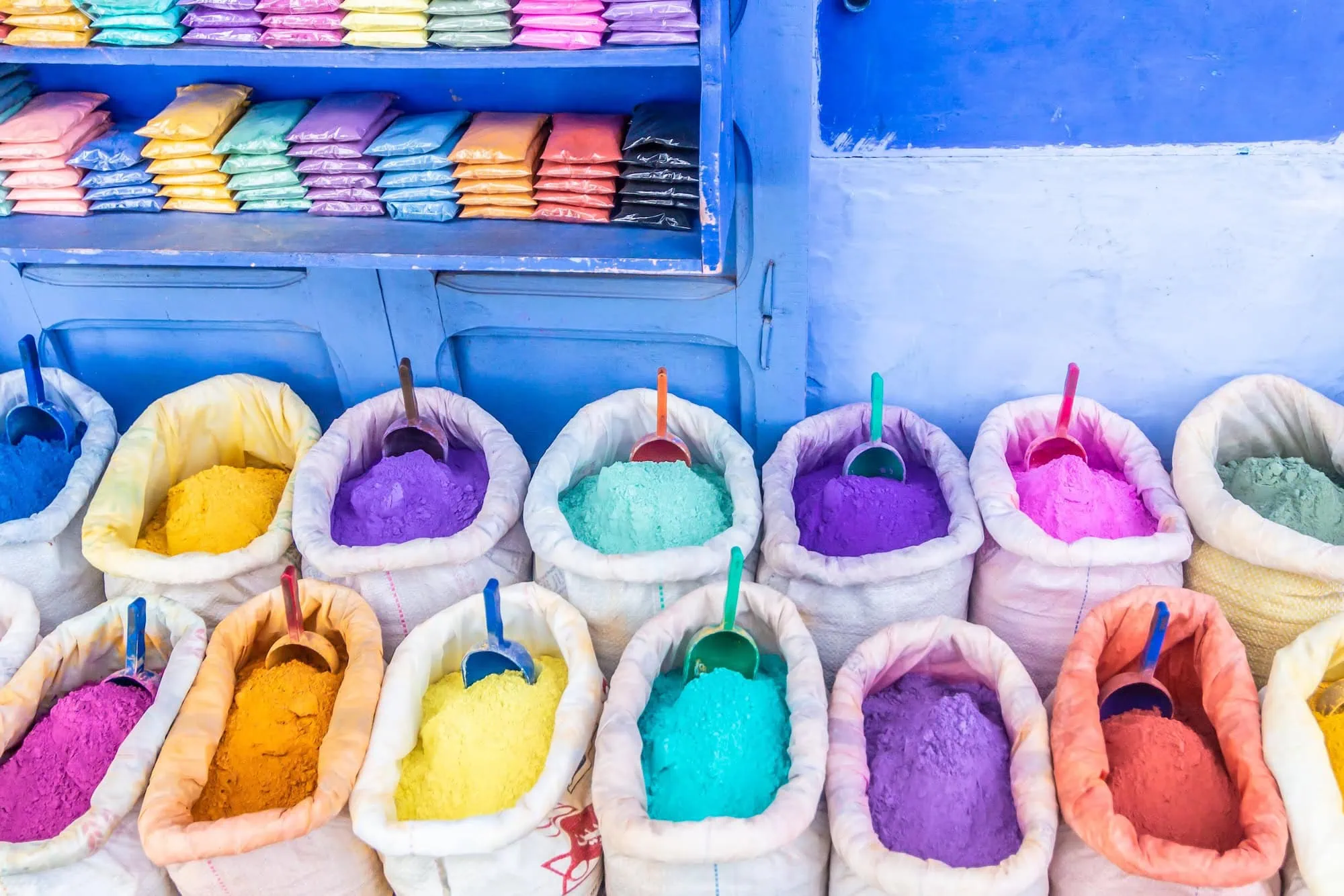 Colorful spices and dyes in white sacks displayed against blue painted walls in Chefchaouen medina