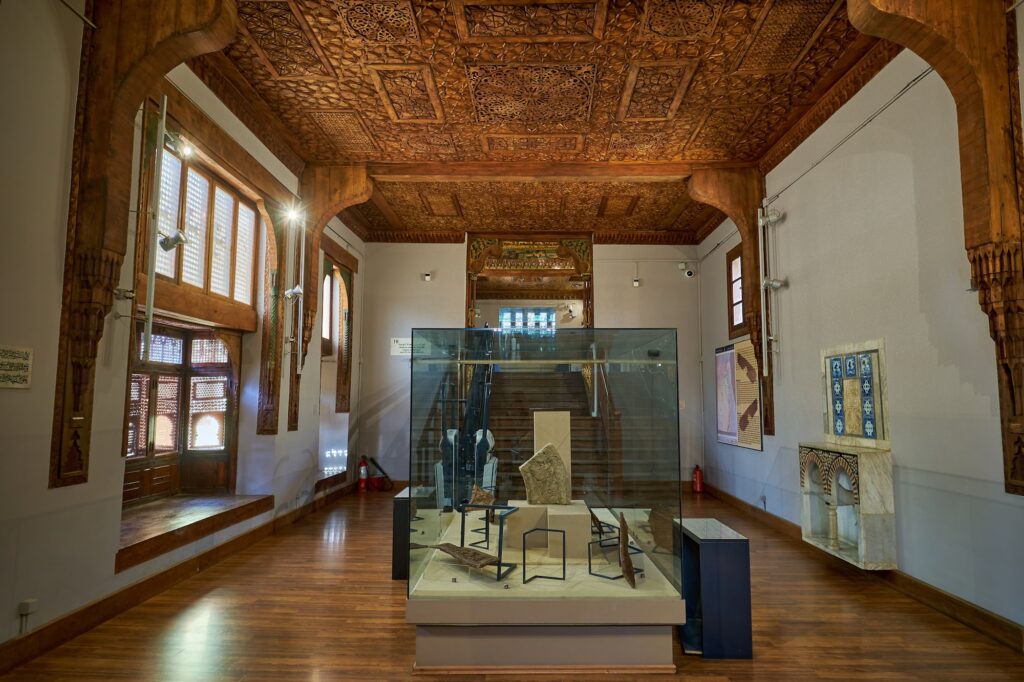 Interior architectural details with carved wooden ceiling, arched openings, display cases, and polished wooden floors inside the Coptic Museum, Cairo