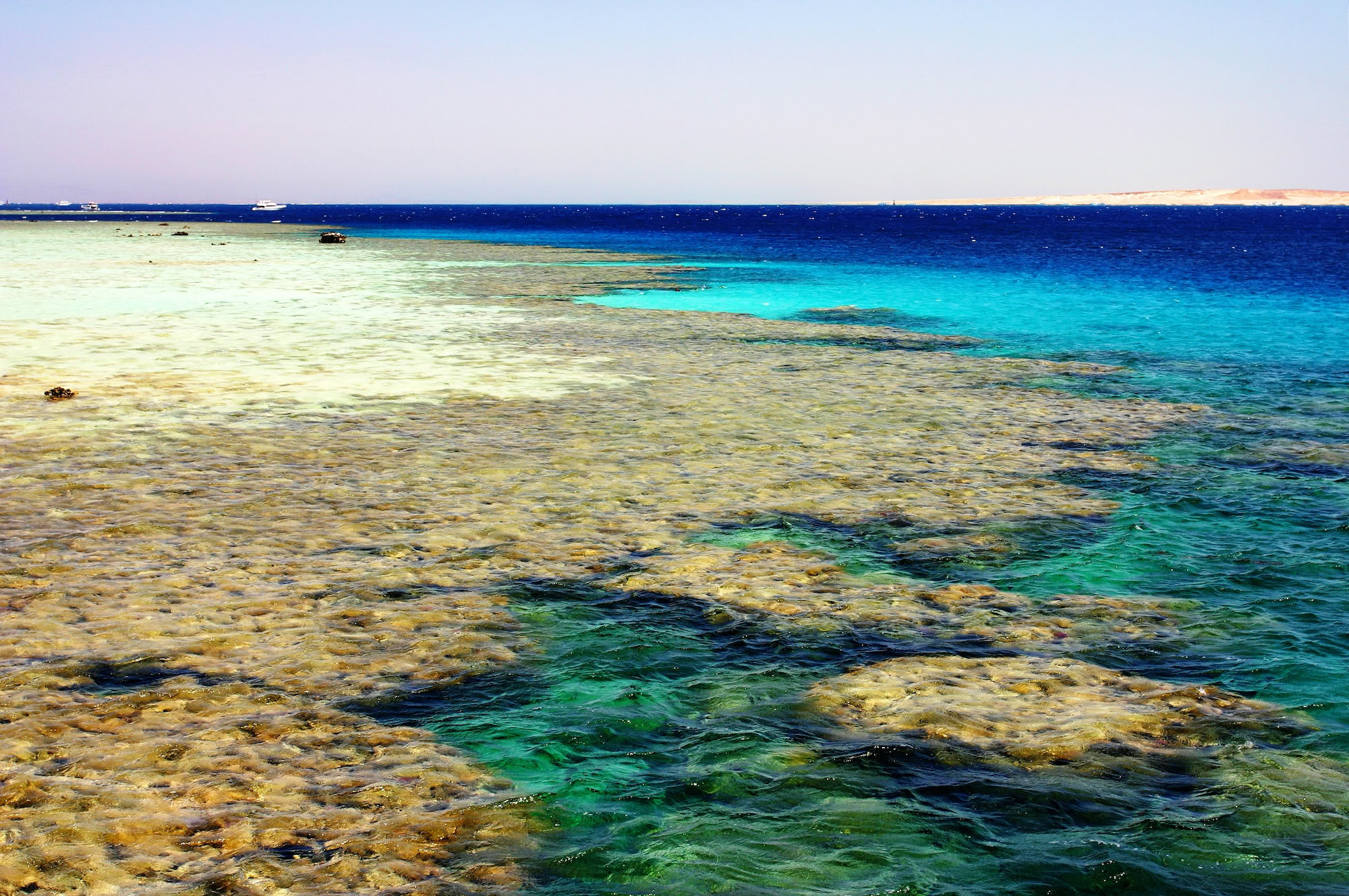 Horseshoe-shaped coral reef lagoon in the Red Sea with turquoise waters and boats