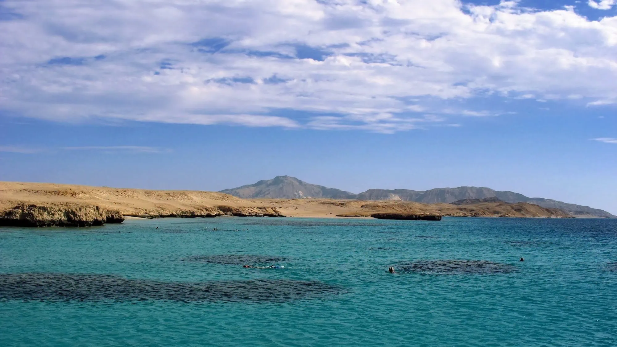 Family snorkeling in crystal clear Red Sea waters with coral reefs visible below